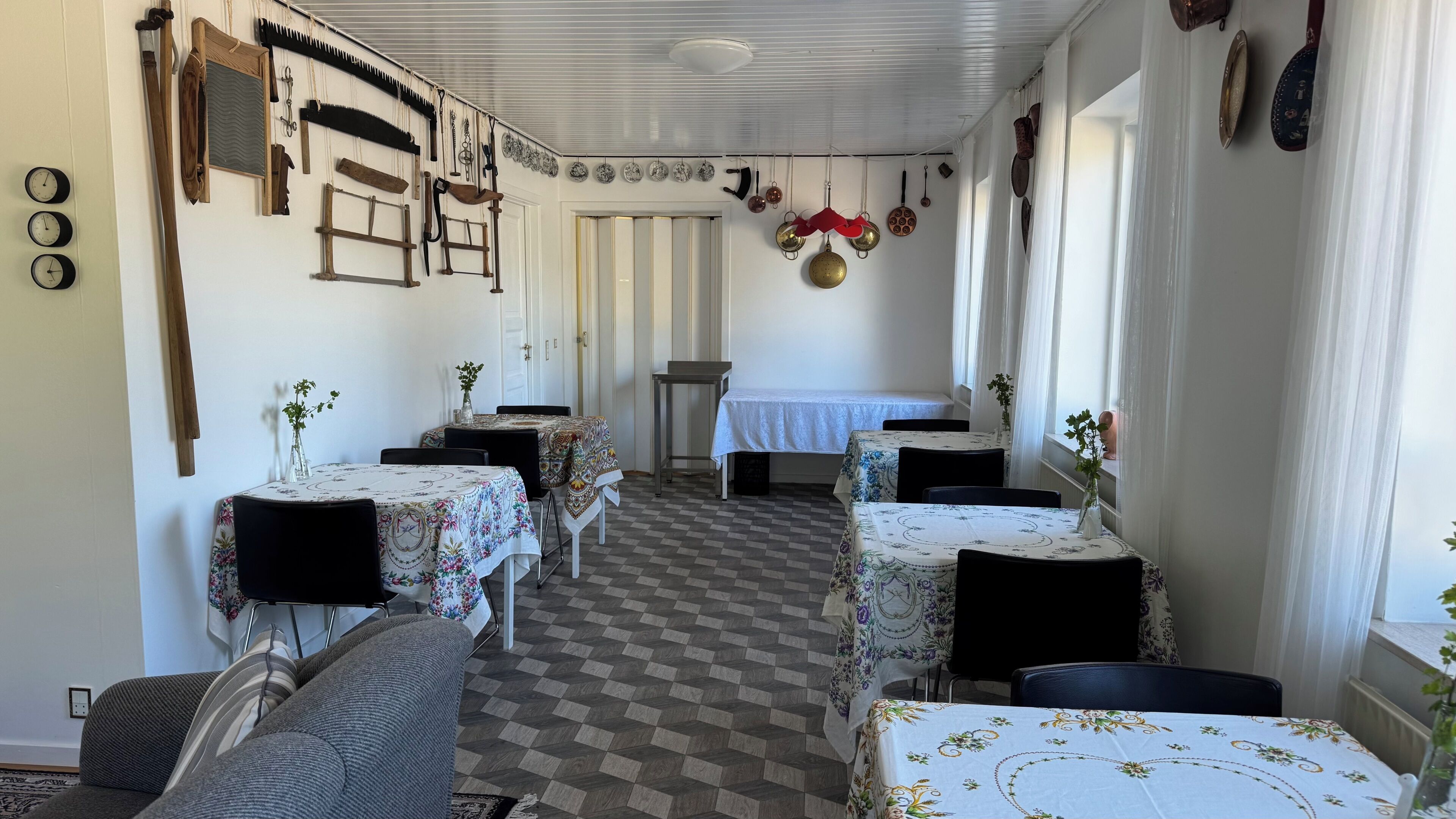 A dining area with tables set for four, a checkered floor, and a view of the dining room through a doorway.
