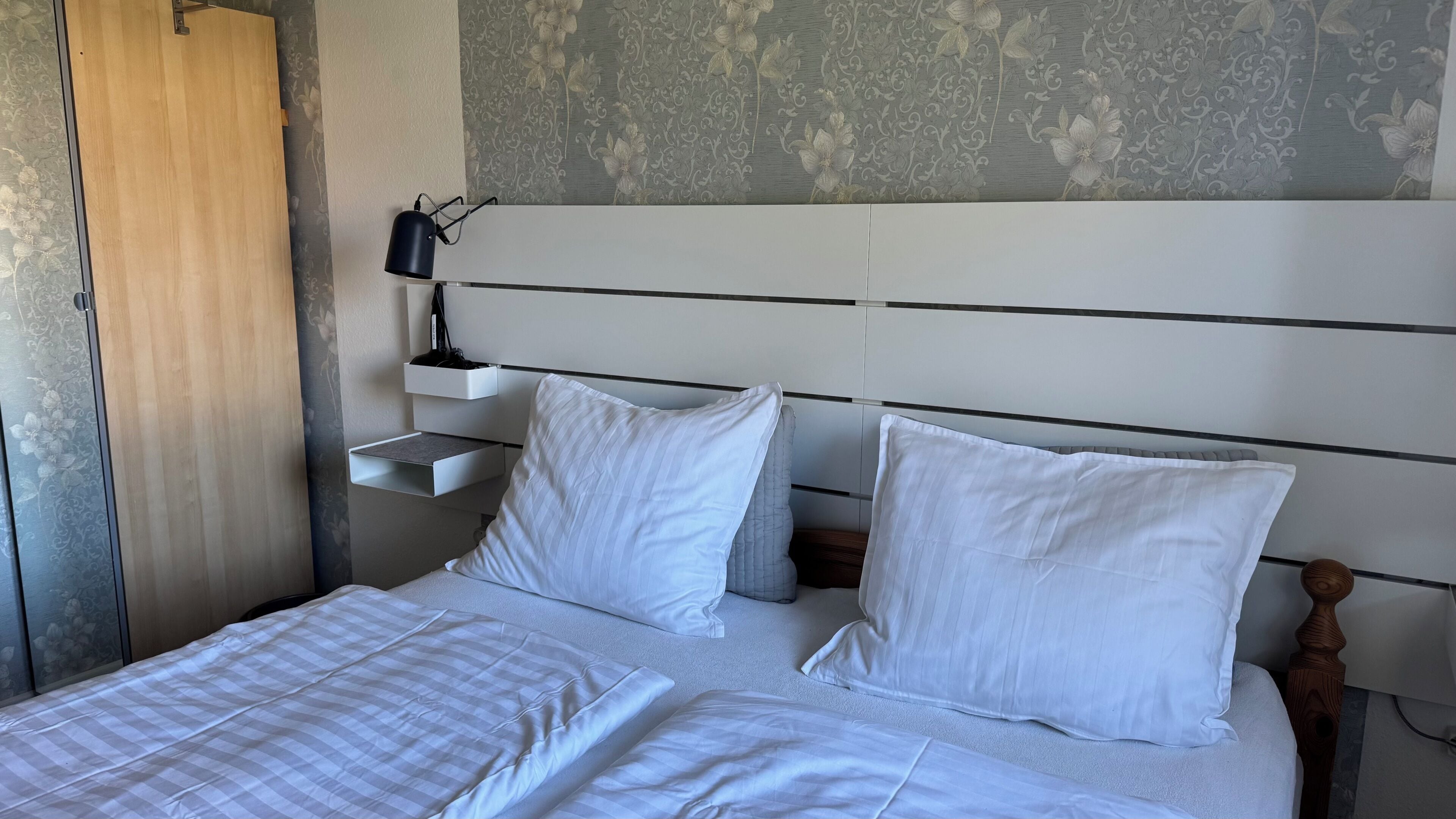 A bed with white bedding, a wooden headboard, and a bedside table with a lamp.