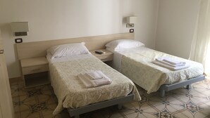 Ein Hotelzimmer mit zwei Einzelbetten, einem Nachttisch, einer Wanduhr und einer Steckdose.