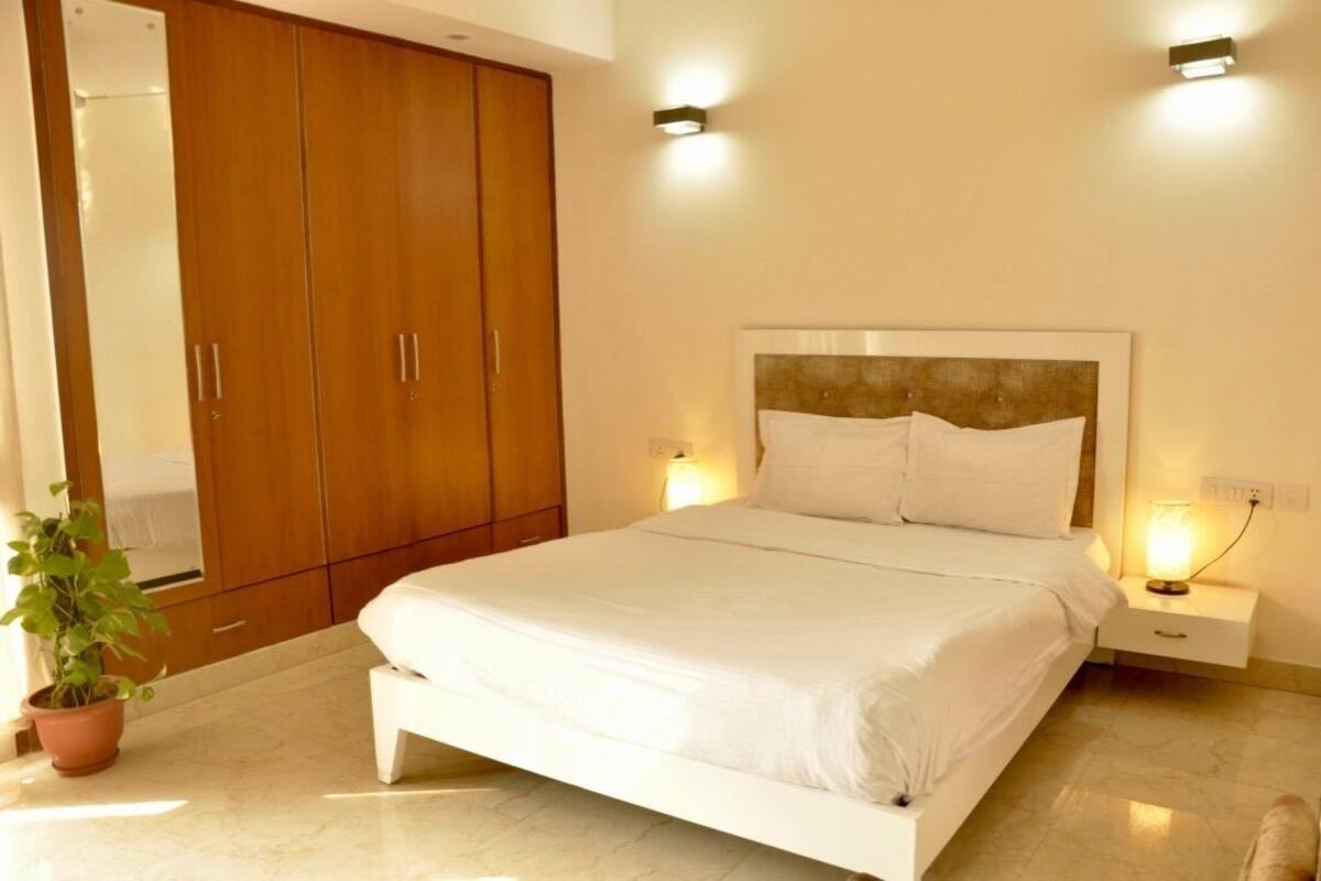 A bedroom with a bed, a nightstand, a potted plant, and a wardrobe.