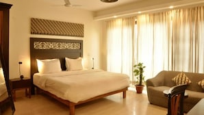 Habitación de hotel con una cama grande, un sofá, un ventilador de techo y una ventana con cortinas.