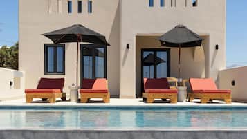 A modern building with a pool, lounge chairs, and umbrellas.