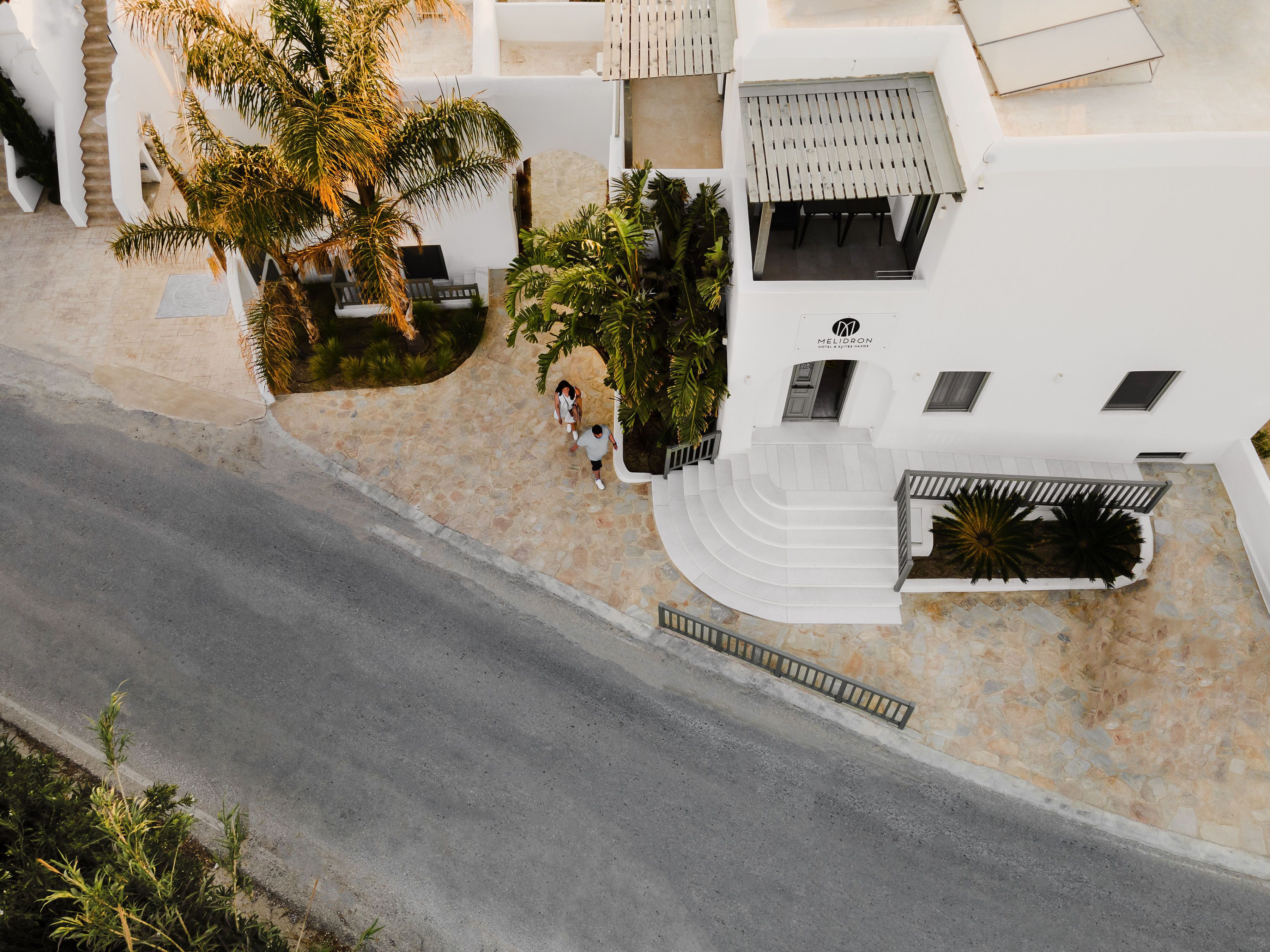 Un bâtiment blanc avec un escalier menant à une zone abritée, entouré de verdure et d’une zone pavée.