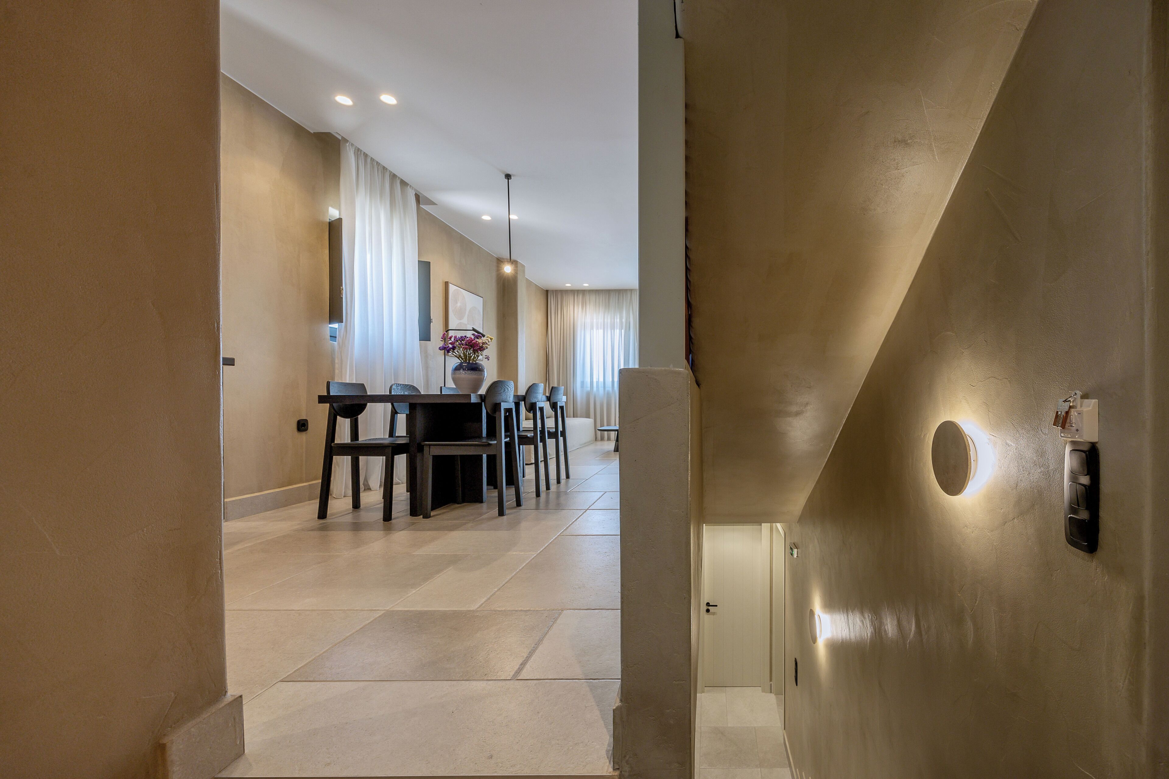 A modern interior with a dining area, a staircase, and a door with a light switch.