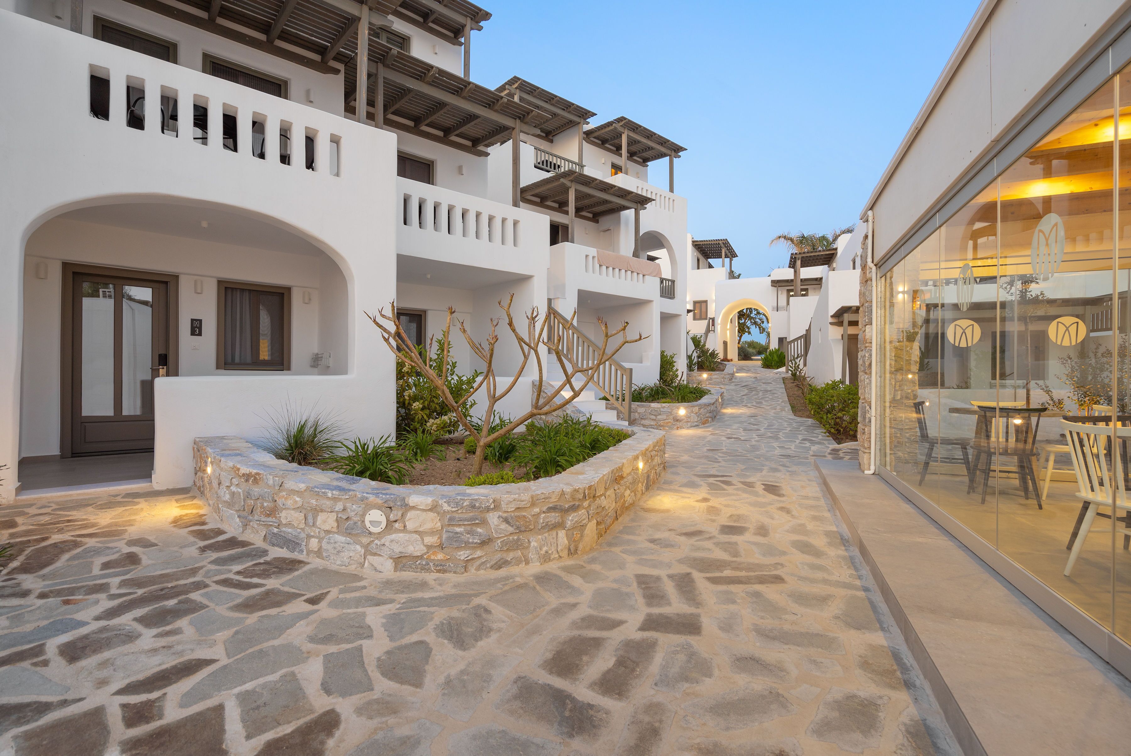 A stone-paved pathway leading to a building with white walls and balconies.