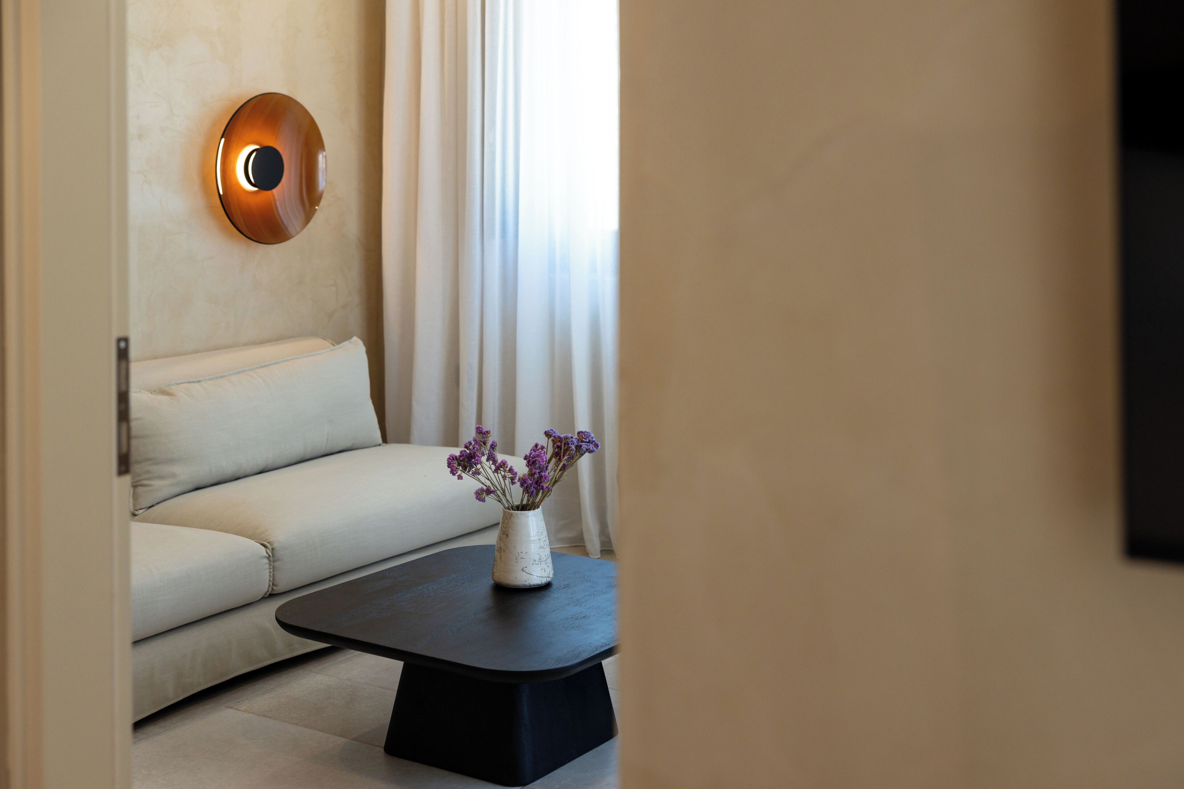 Un salon moderne avec un canapé, une table basse ornée d’un vase de fleurs et un luminaire fixé au mur.