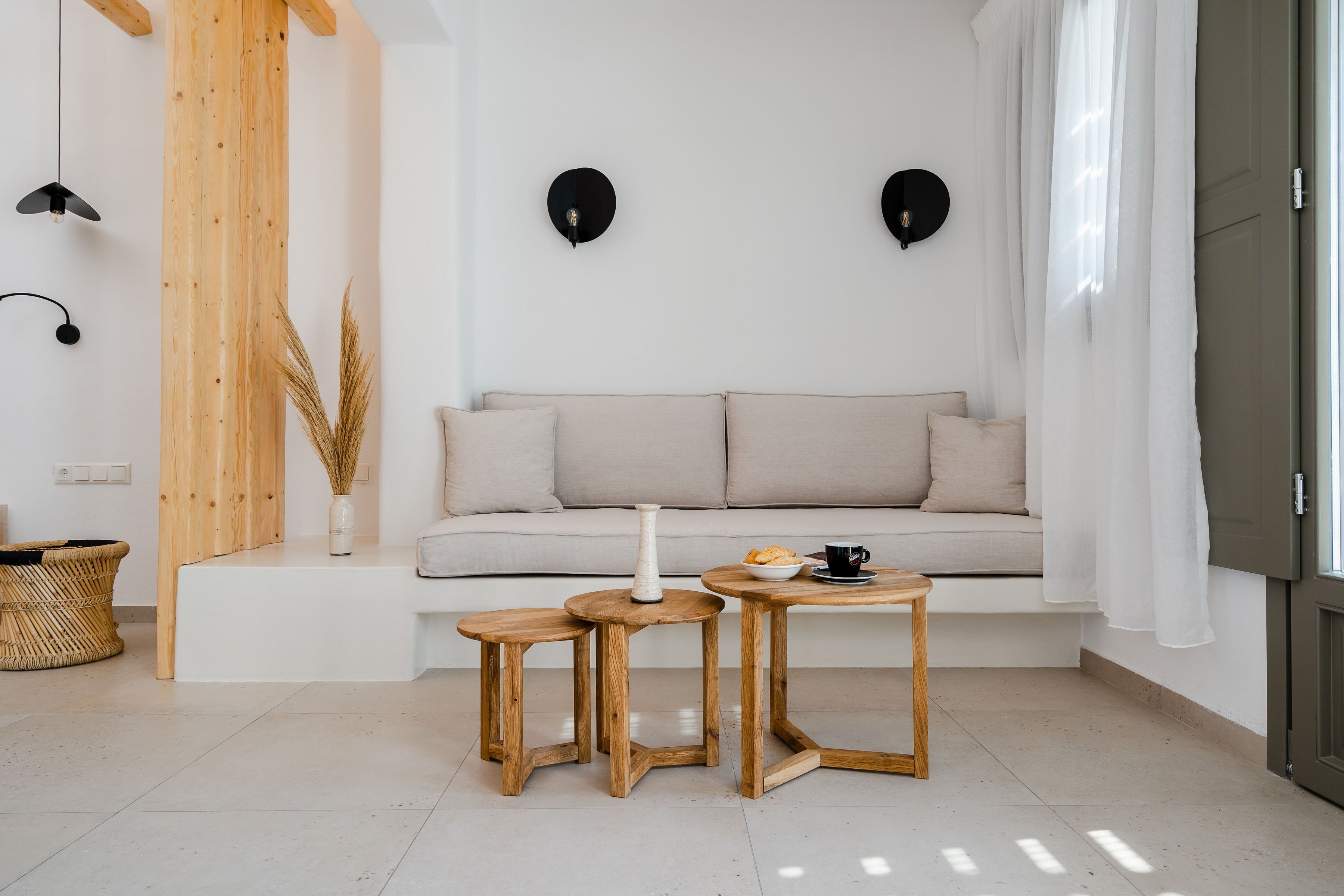 A modern living room with a sofa, two wooden side tables, a vase, and a basket.