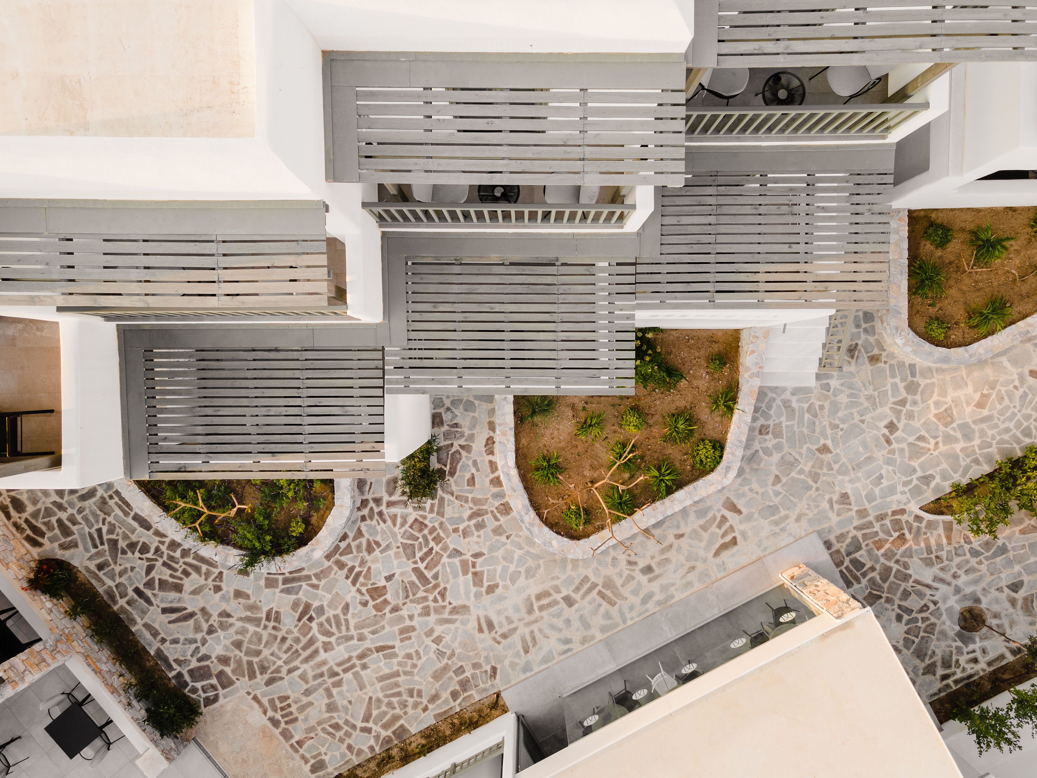 Luchtbeeld van een modern gebouw met een patio met stenen bestrating, witte balkons en groene beplanting.