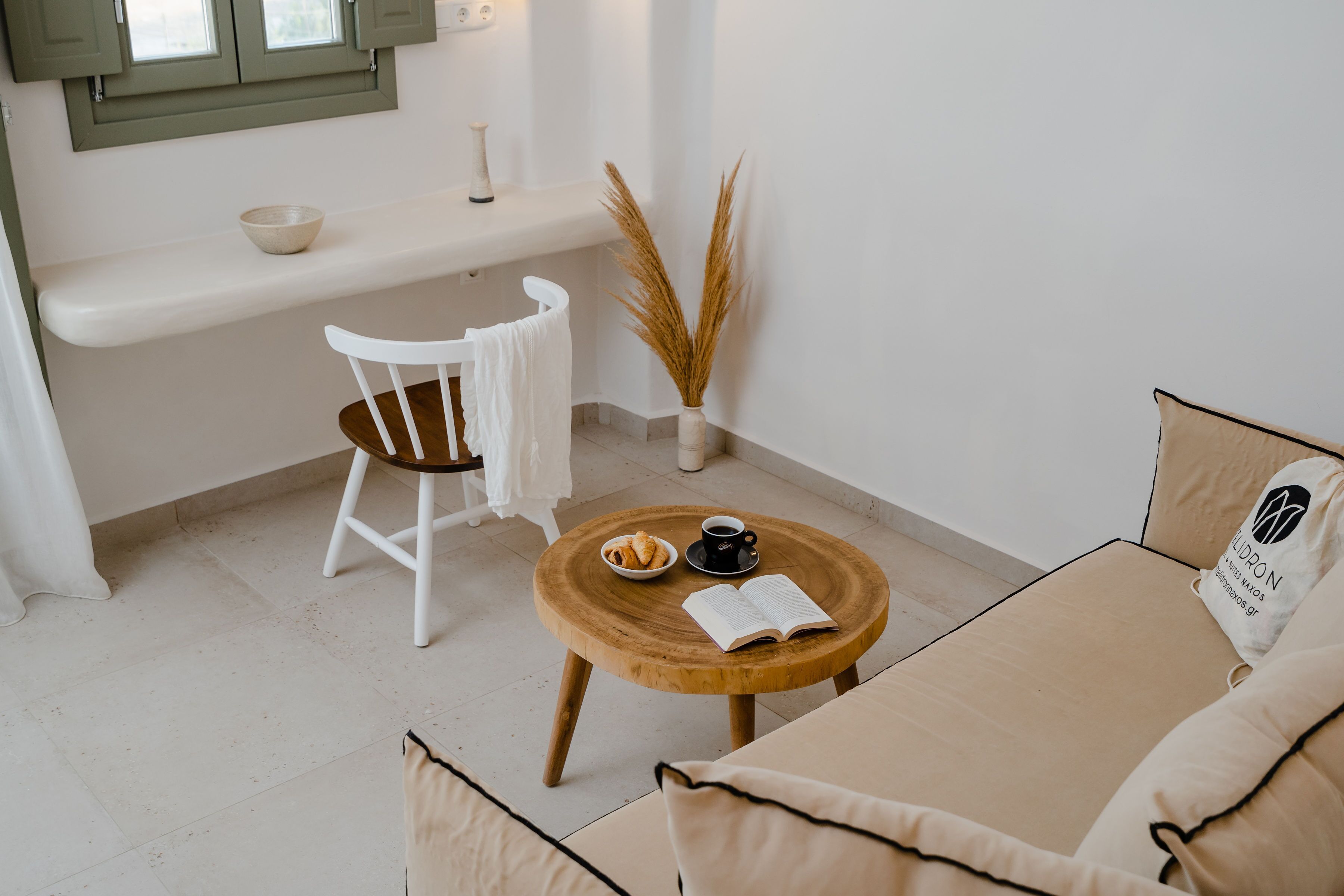 A cozy room with a wooden table, a white chair, a sofa, and a small kitchen area with a bowl and a cup.