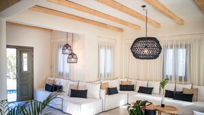 Een moderne woonkamer met een hoekbank, hanglampen en een houten plafond.