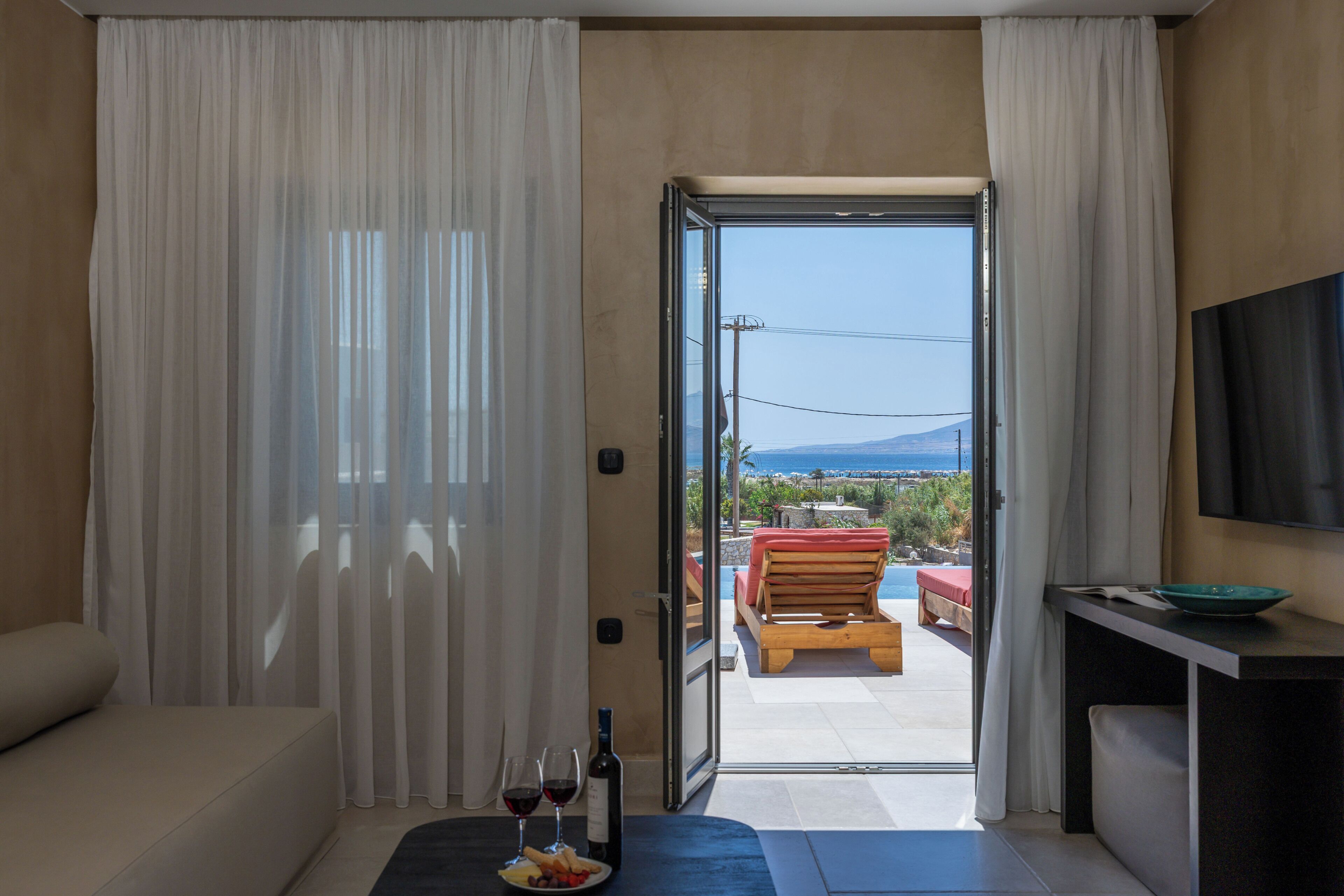 Una habitación con sofá, una mesa de comedor con un bol y copas de vino, y vistas a una piscina y zona de estar exterior.