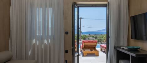 Una habitación con sofá, una mesa de comedor con un bol y copas de vino, y vistas a una piscina y zona de estar exterior.