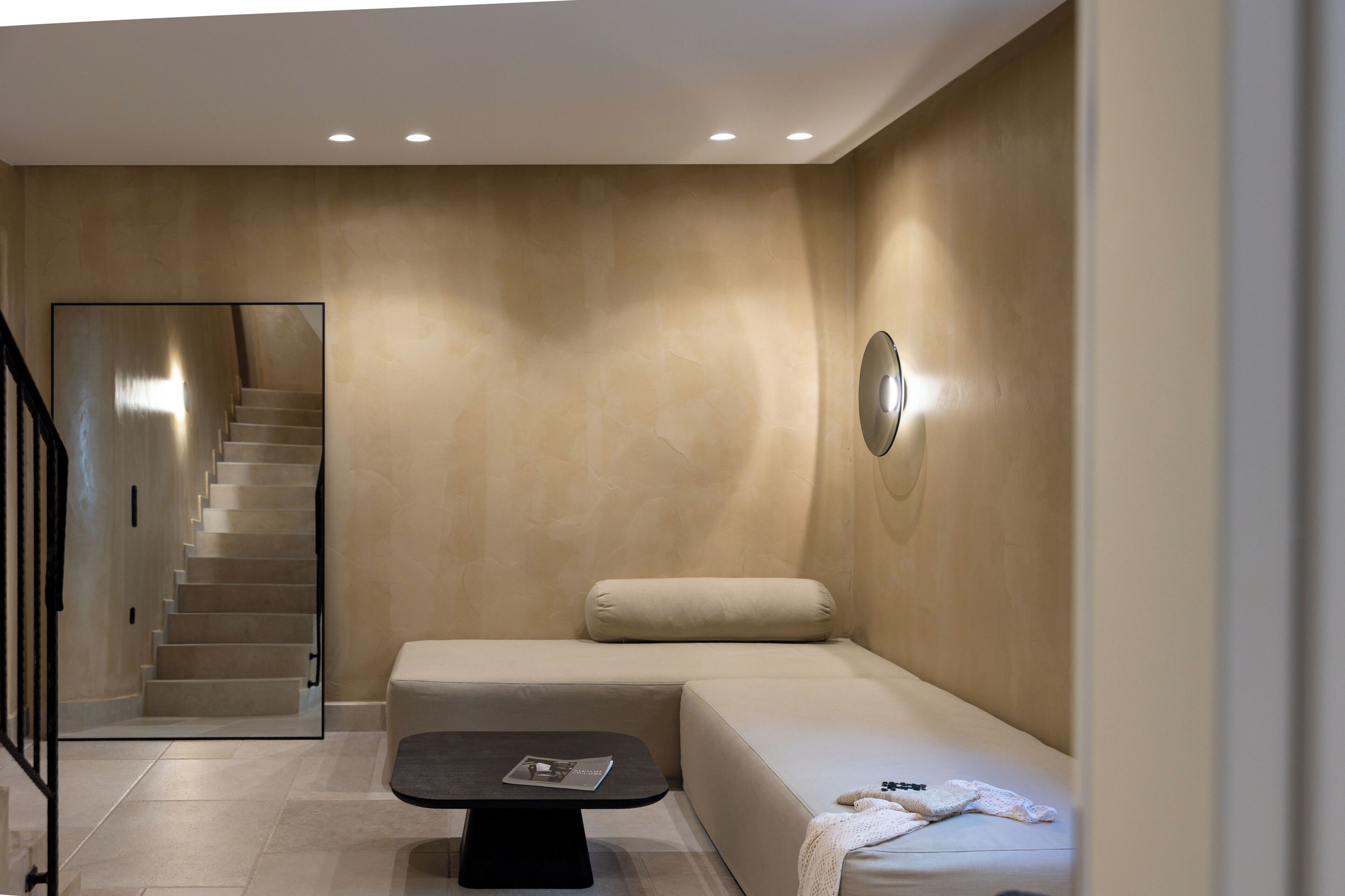 A modern interior with a staircase, a sofa, a small table, and a wall-mounted light fixture.