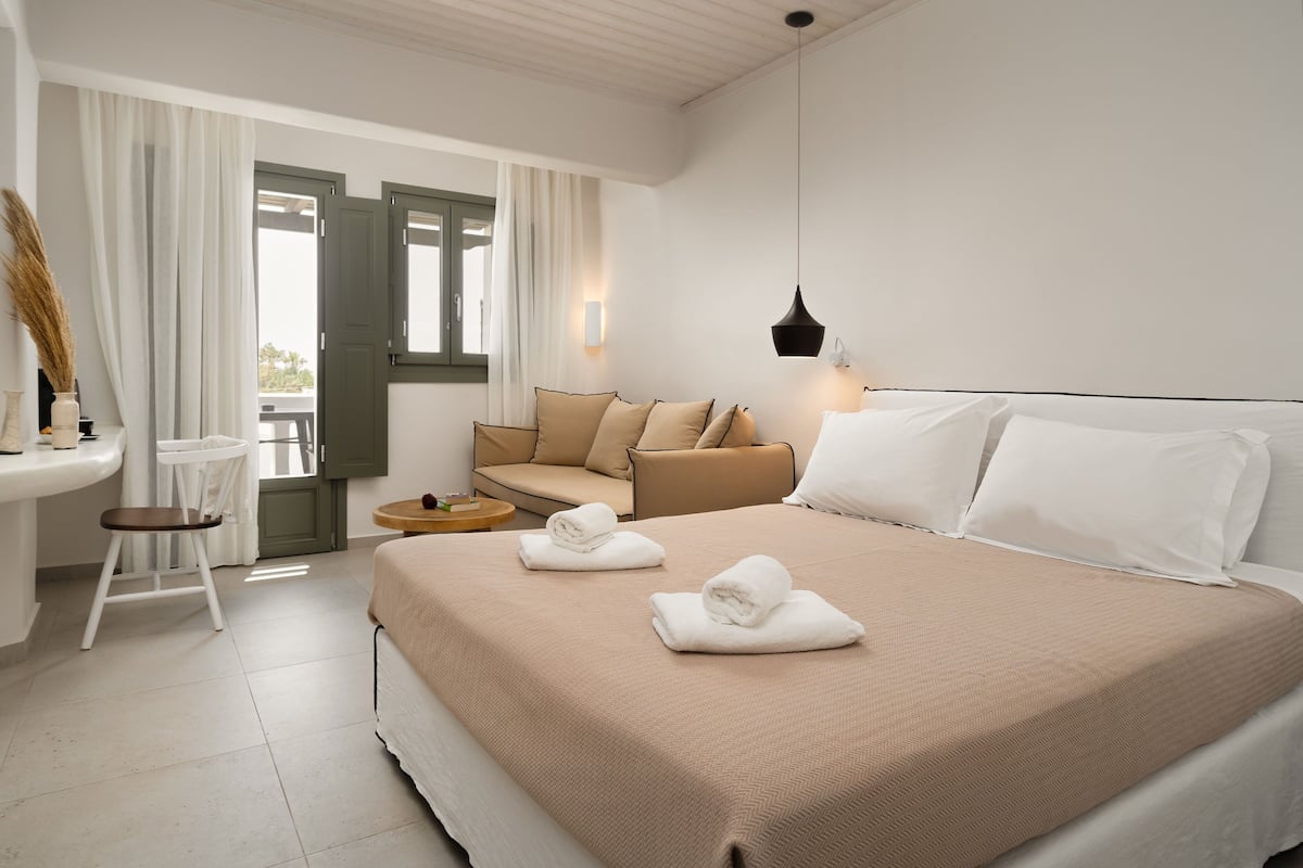 A hotel room with a bed, a sofa, a small table, and a chair.