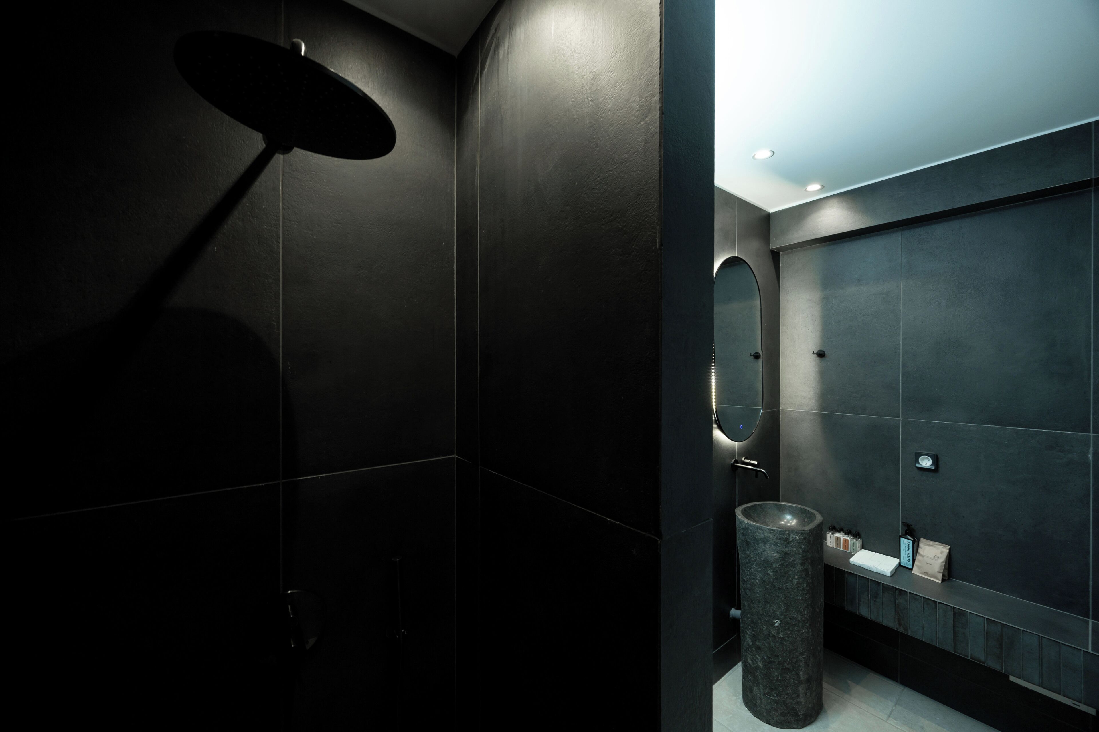 A modern bathroom with dark tiles, a round mirror, and a cylindrical sink.