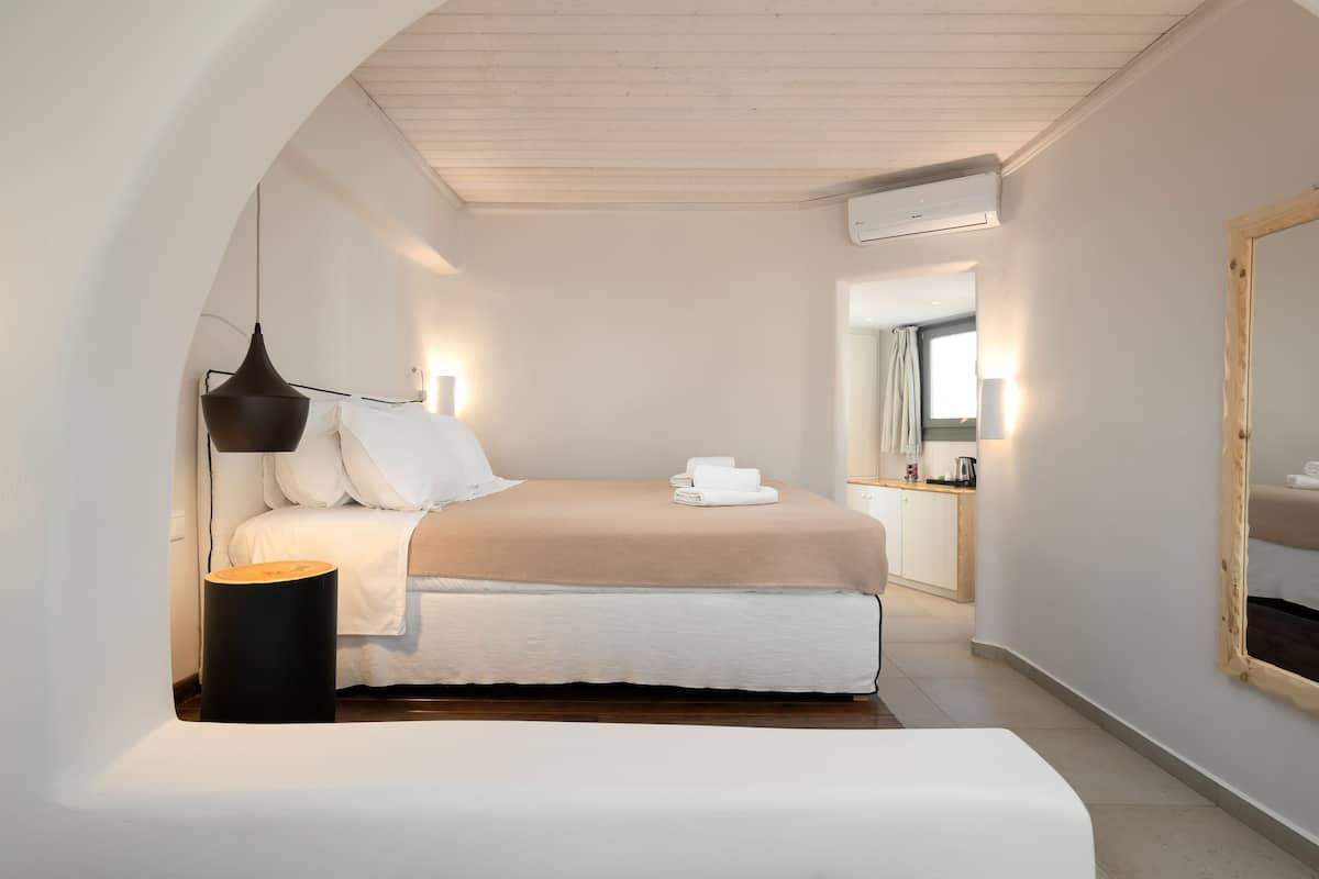 A narrow, well-lit bedroom with a bed, bedside lamp, and a mirror.