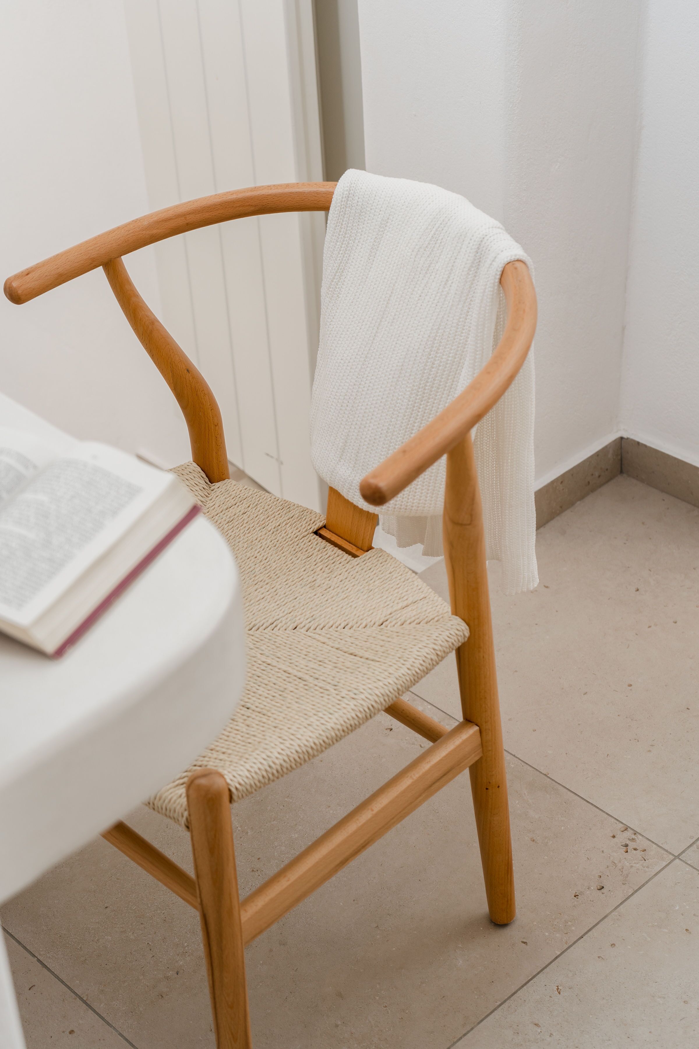 Ein hölzerner Stuhl mit gewebtem Sitz und Rückenlehne, neben einem weißen Tisch mit einem Buch.