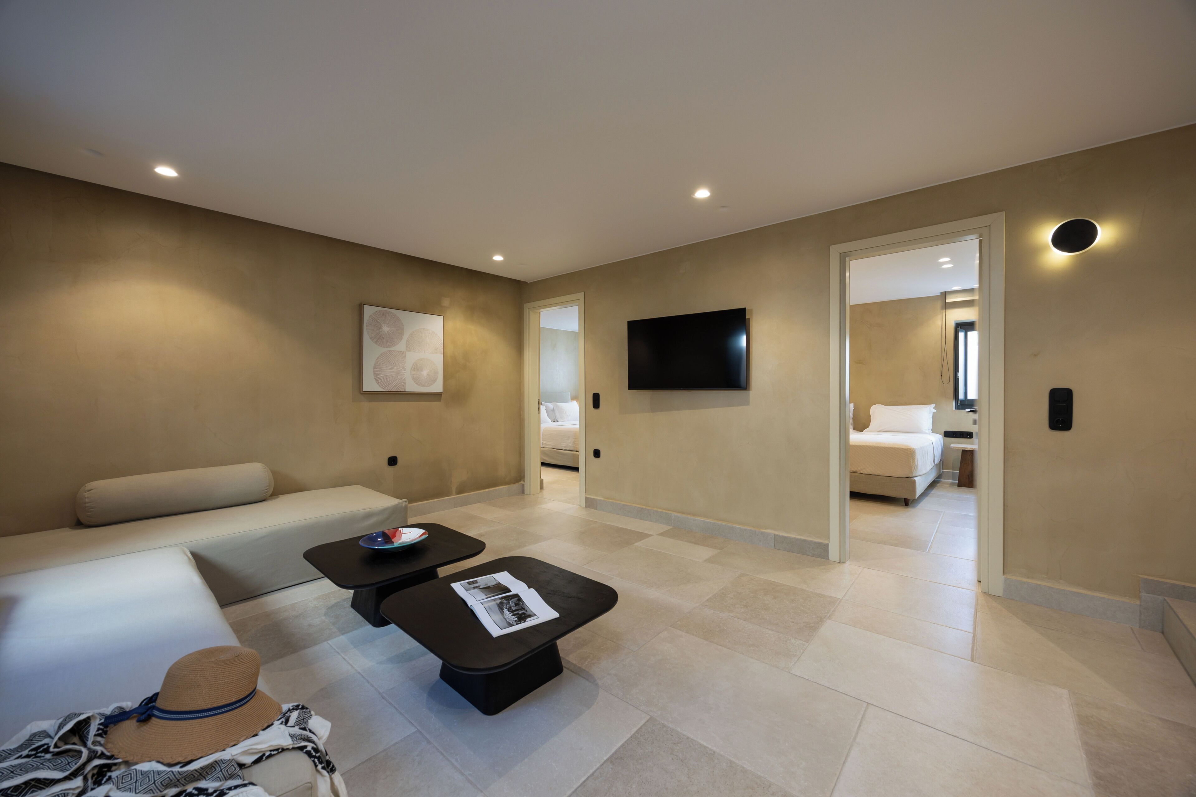 A modern living room with a sofa, a coffee table, a flat-screen TV mounted on the wall, and a hallway leading to a bedroom.