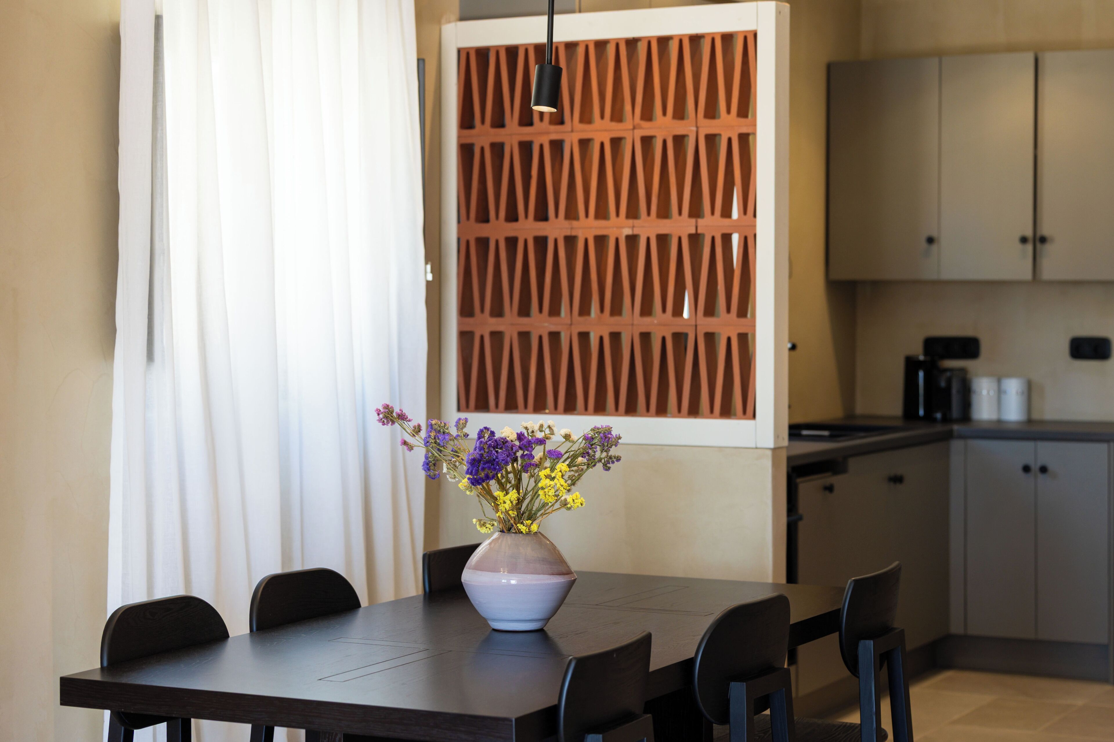 A modern kitchen with a dining table, chairs, a vase with flowers, and a wooden partition.