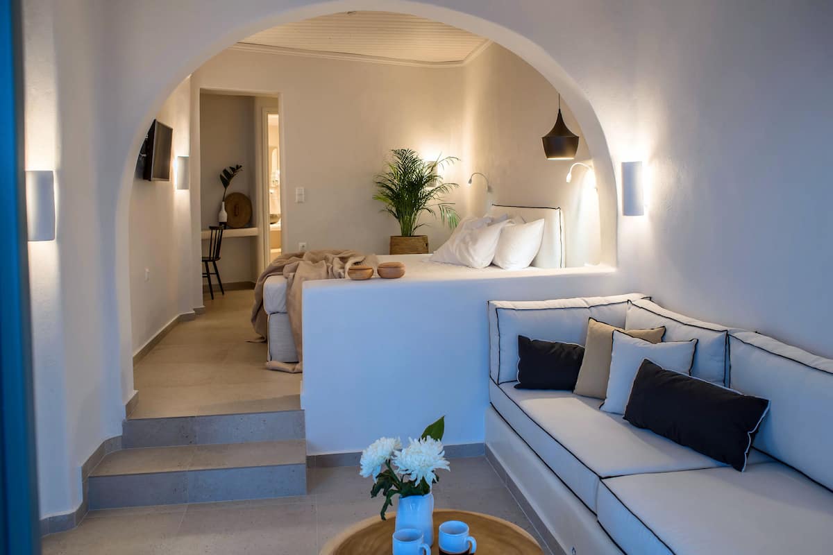 A modern, minimalist living room with a sofa, a coffee table with a vase of flowers, and a staircase leading to another room.