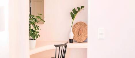 A minimalist room with a black chair, a potted plant, a woven wall hanging, and a small mirror.