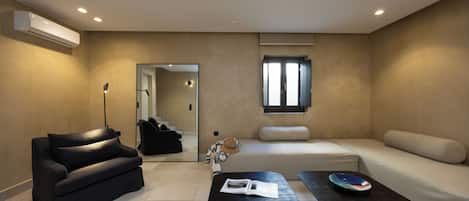 Una sala de estar moderna con un sofá negro, un sofá beige y una mesa de centro negra con una revista.