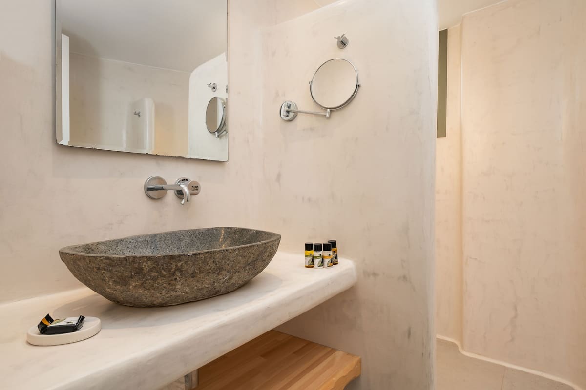 A bathroom with a large stone sink, a mirror, a round hand soap dispenser, and a small bottle of liquid soap.