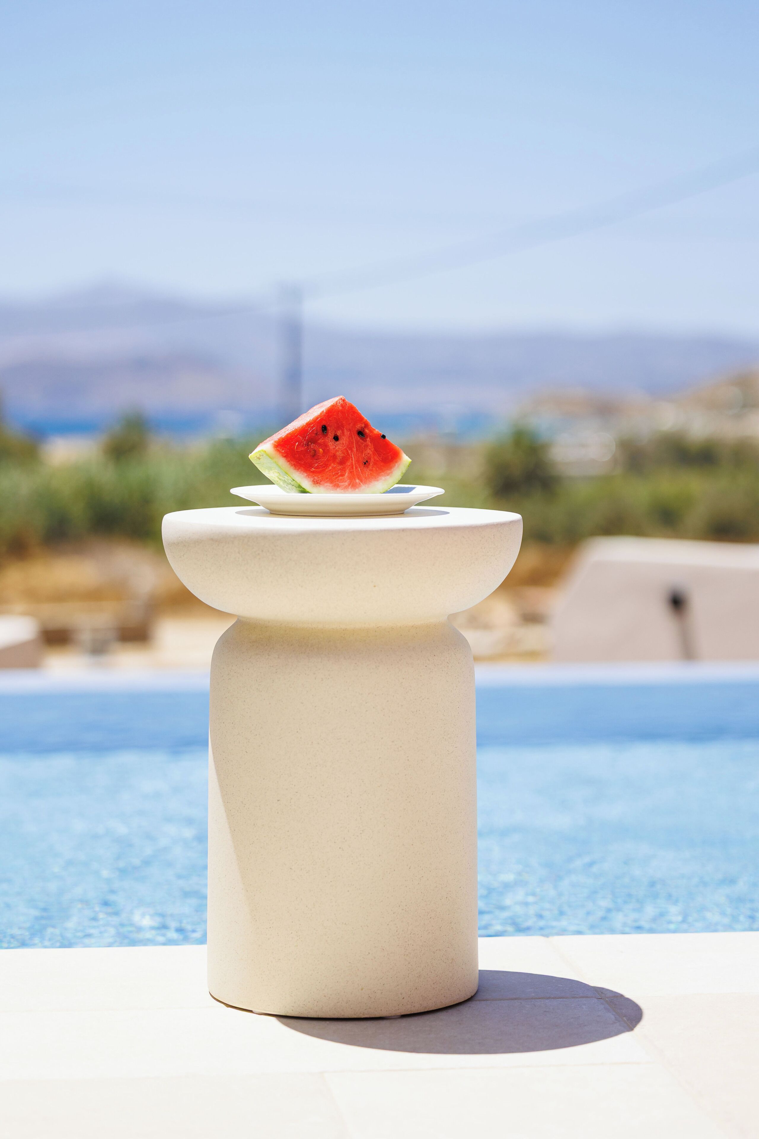 A poolside setting with a white pedestal and a slice of watermelon on top.