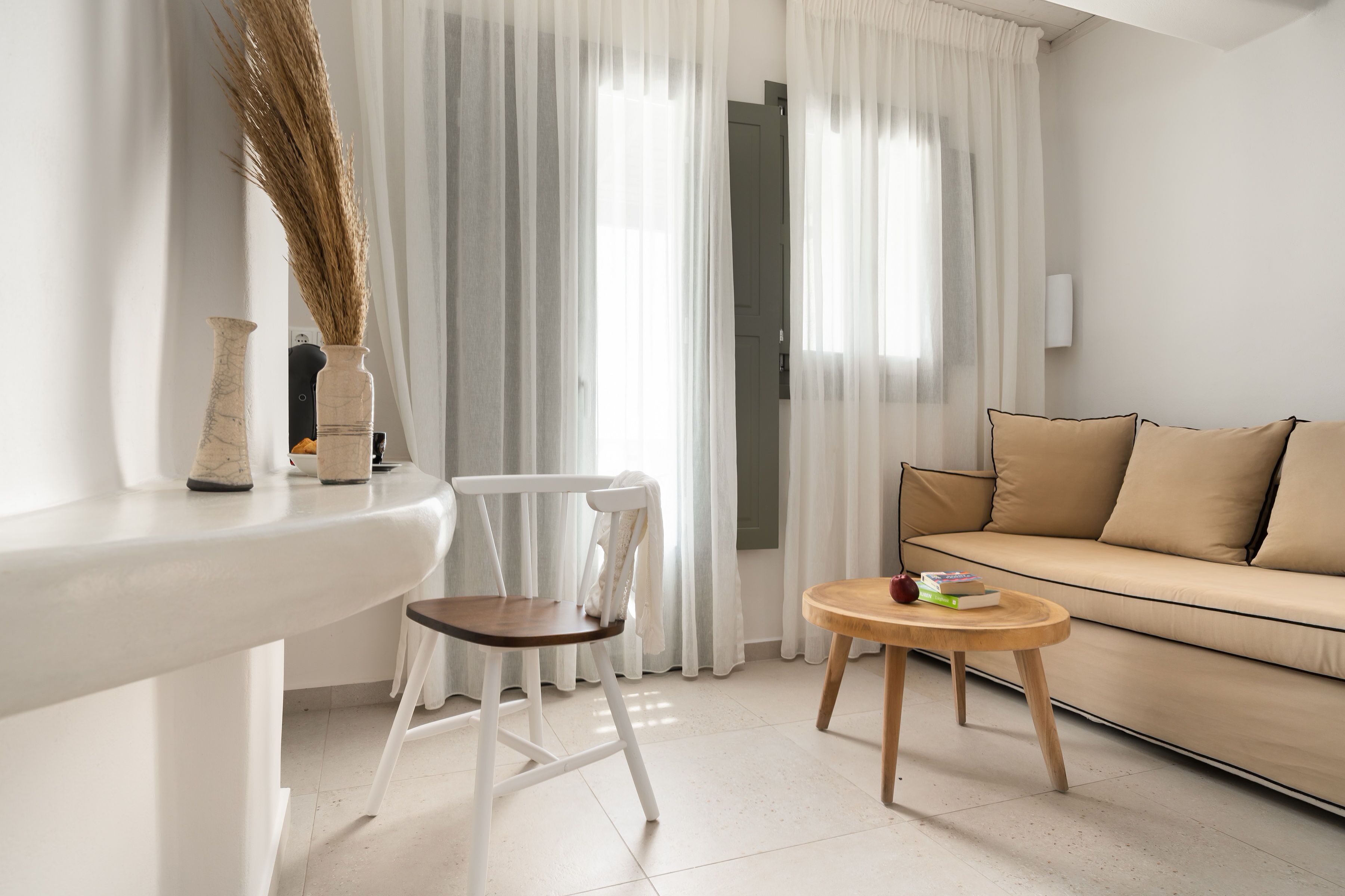 A modern living room with a white sofa, a wooden coffee table, a white chair, and a white side table with a vase and a knife.