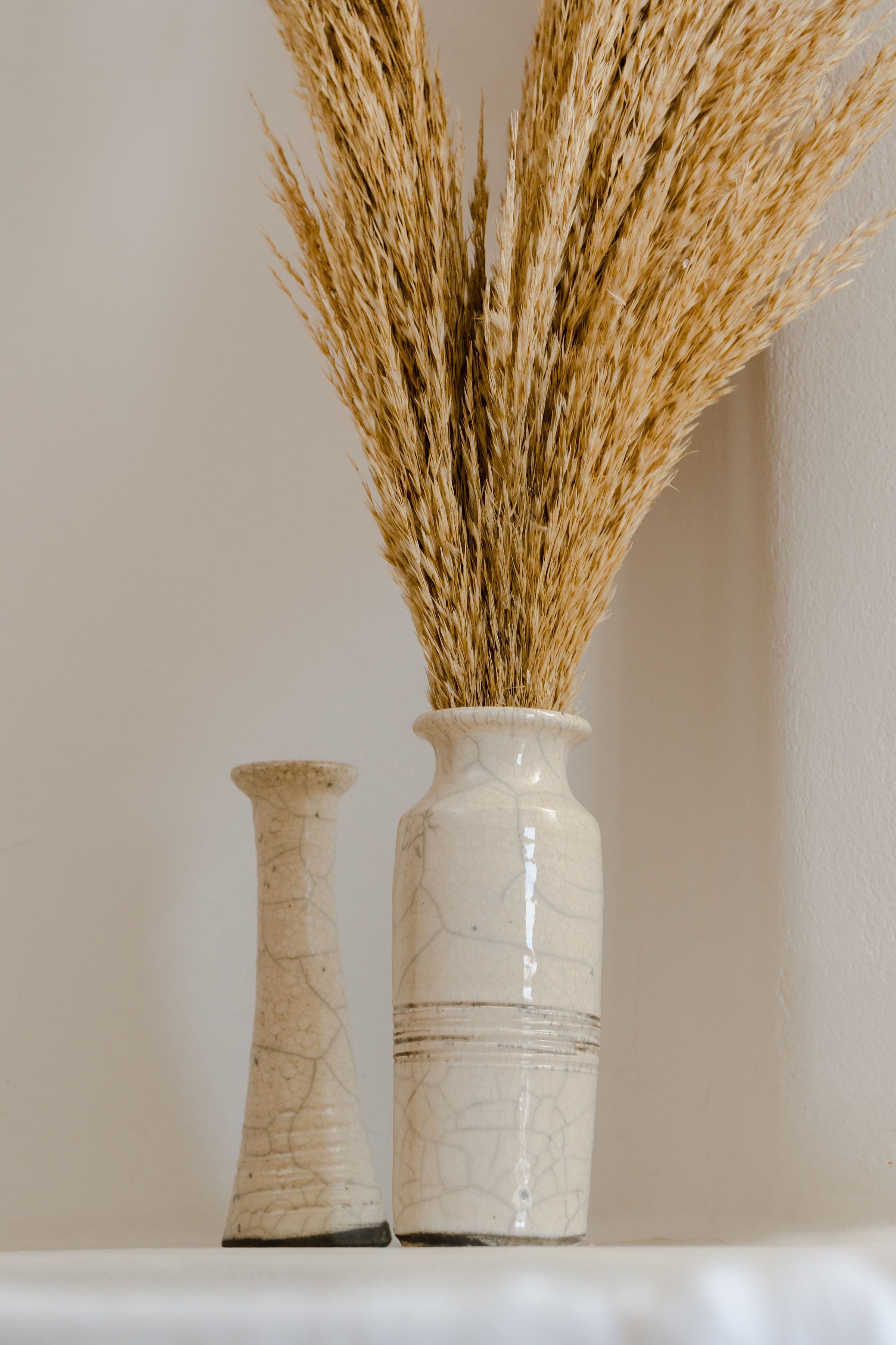 Two white ceramic vases with a crackled texture, one taller than the other, placed on a white surface against a plain wall.