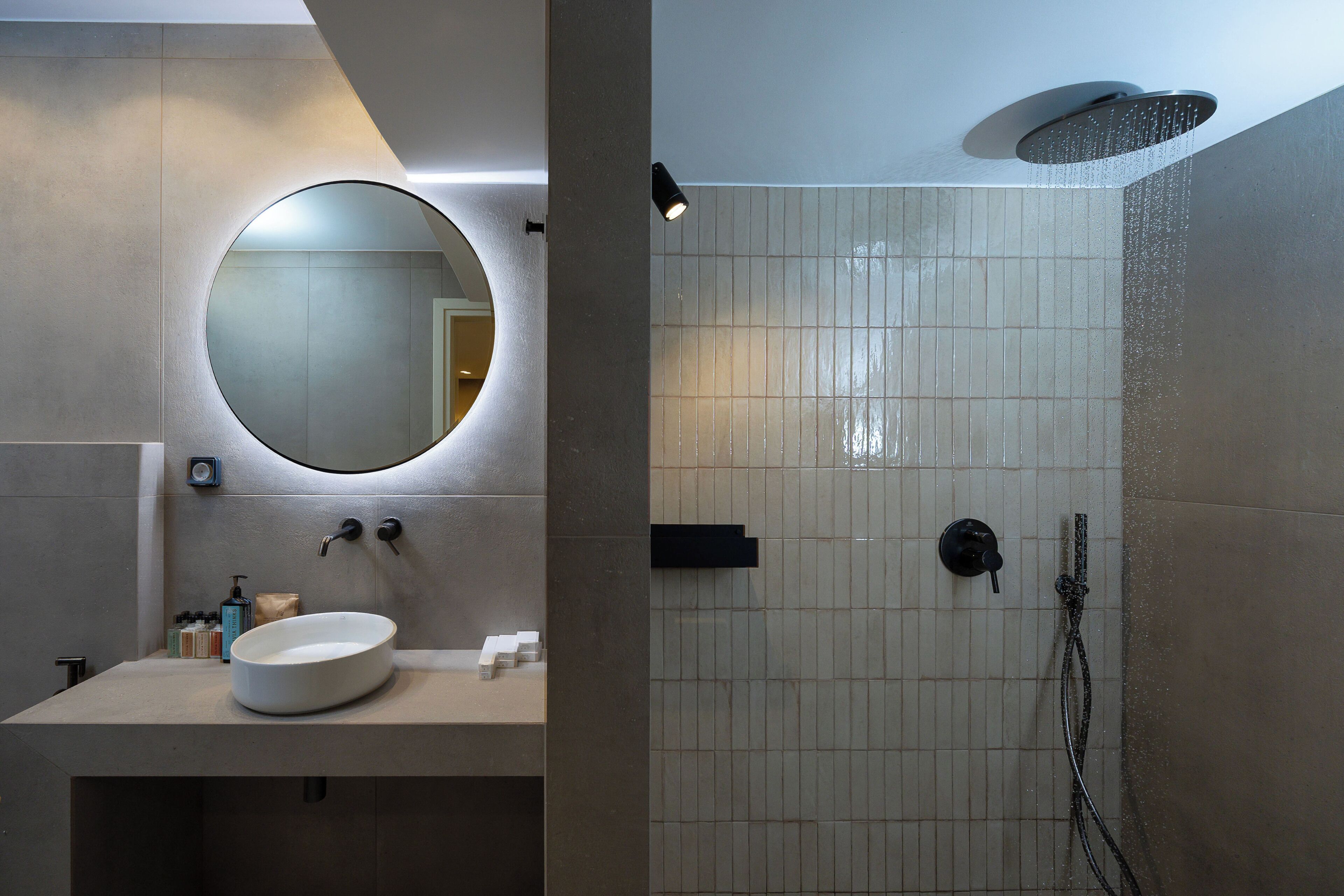 Ein modernes Badezimmer mit rundem Spiegel, Waschbecken und Duschbereich.
