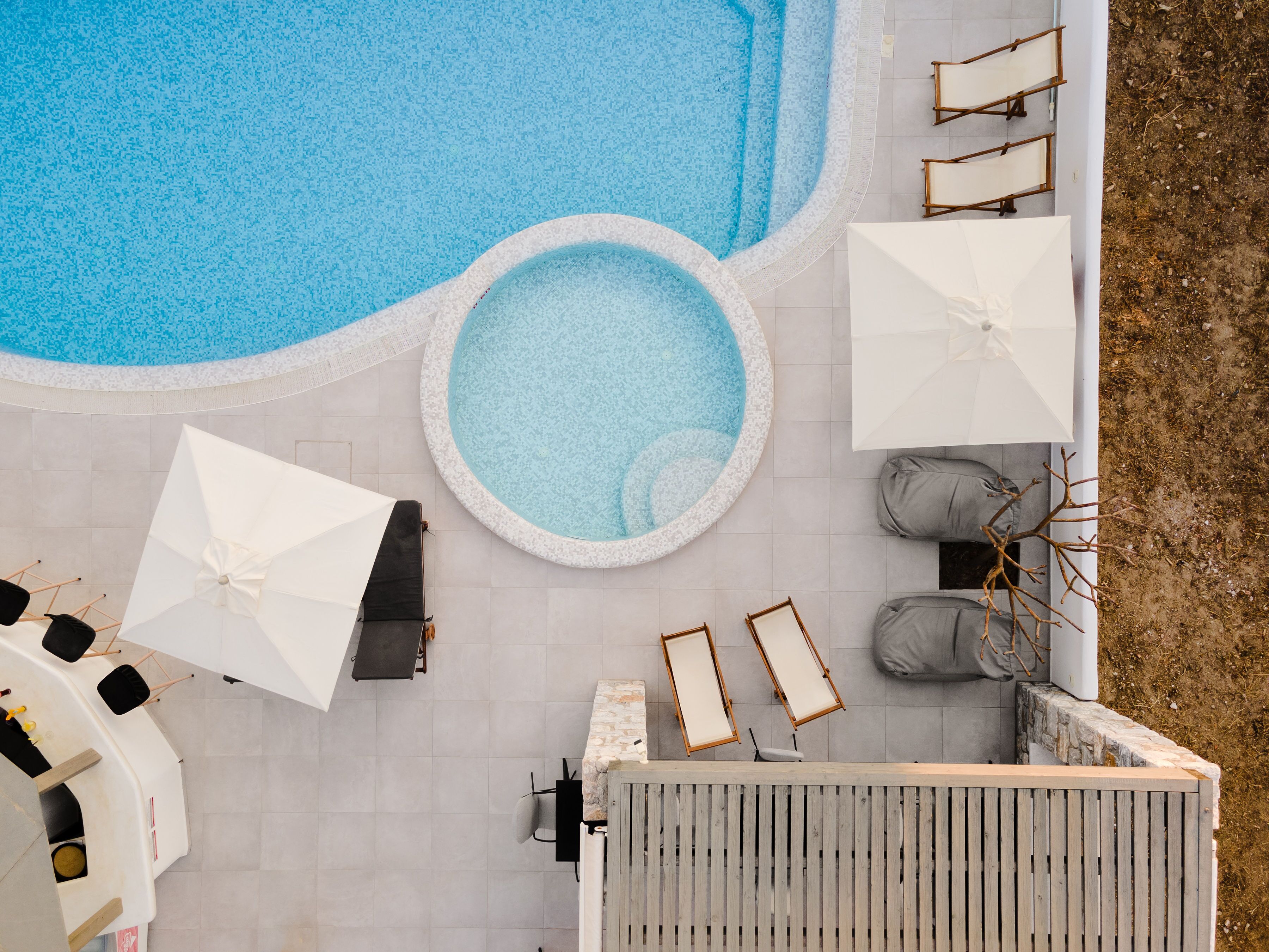 Un área de piscina en la azotea con varios espacios de descanso, sombrillas y una piscina circular pequeña.