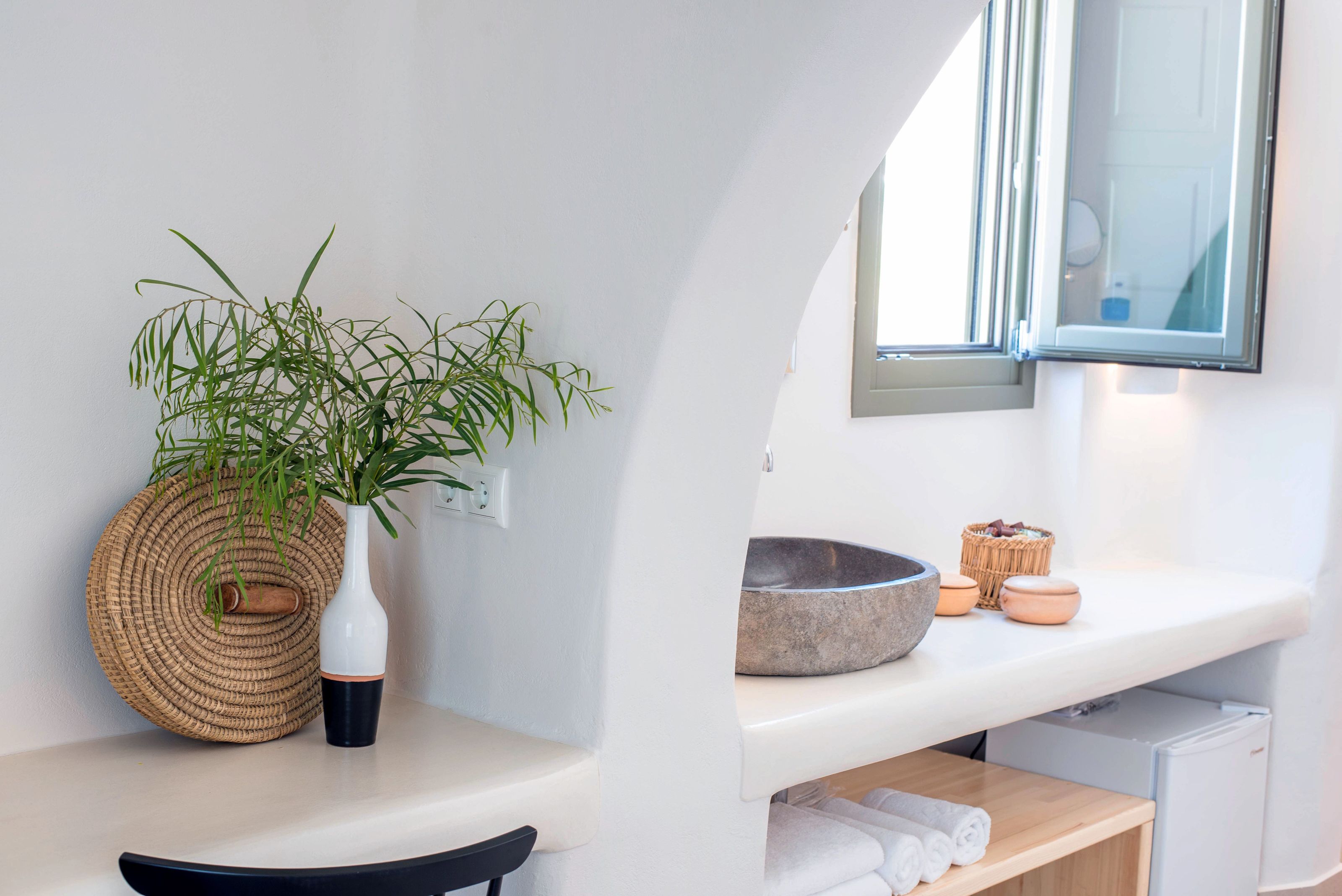 Un baño con un lavabo blanco, un espejo, una planta, una cesta tejida y una pileta de piedra.