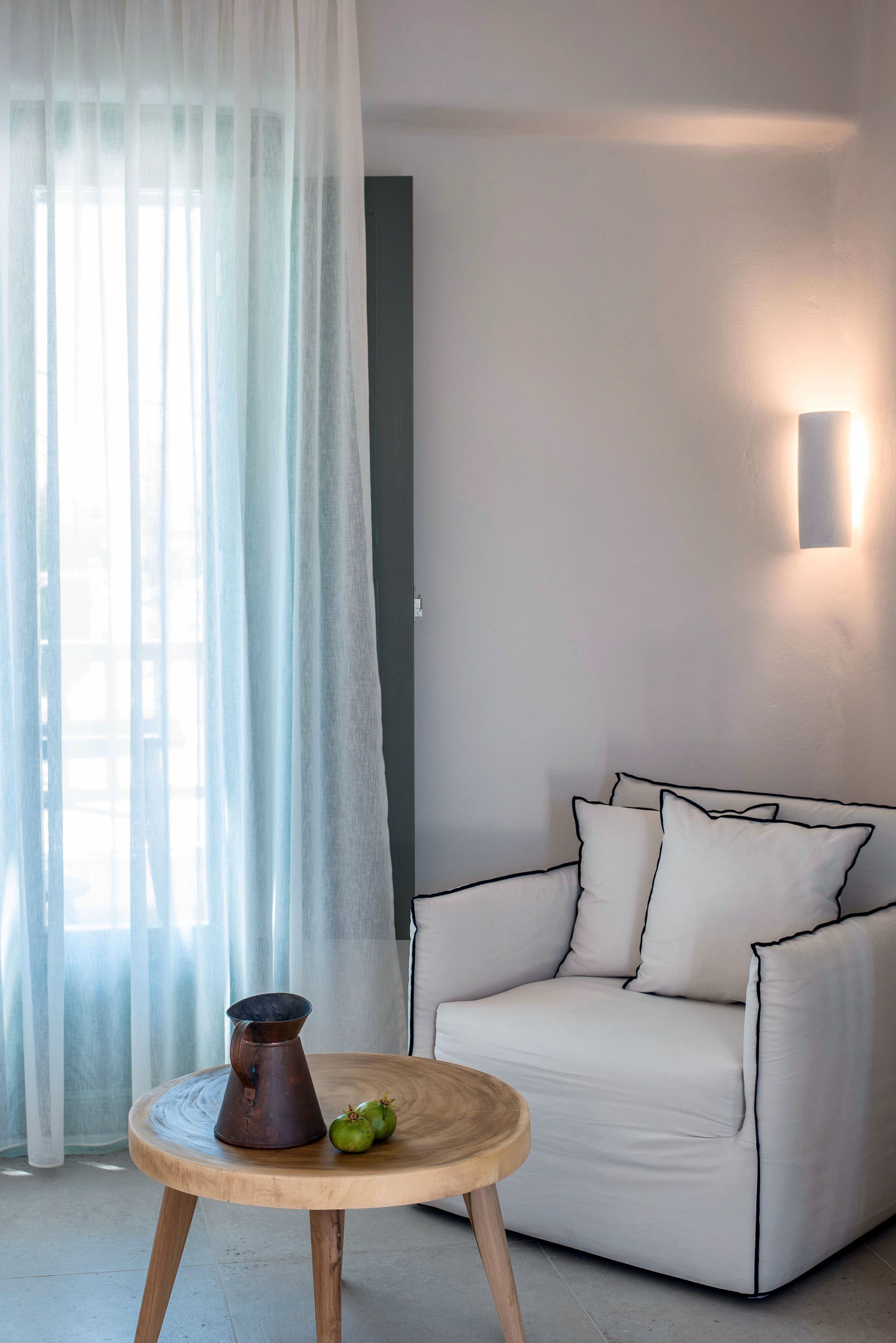 A modern living room with a white sofa, a round wooden table, and a wall-mounted light fixture.