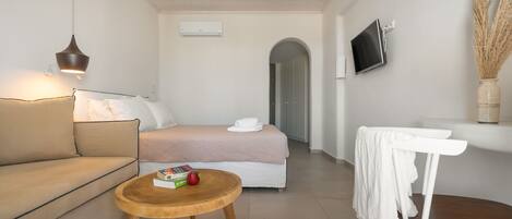 Una habitación de hotel moderna con una cama, un sofá, una mesa de madera, un televisor y un jarrón con plantas secas.