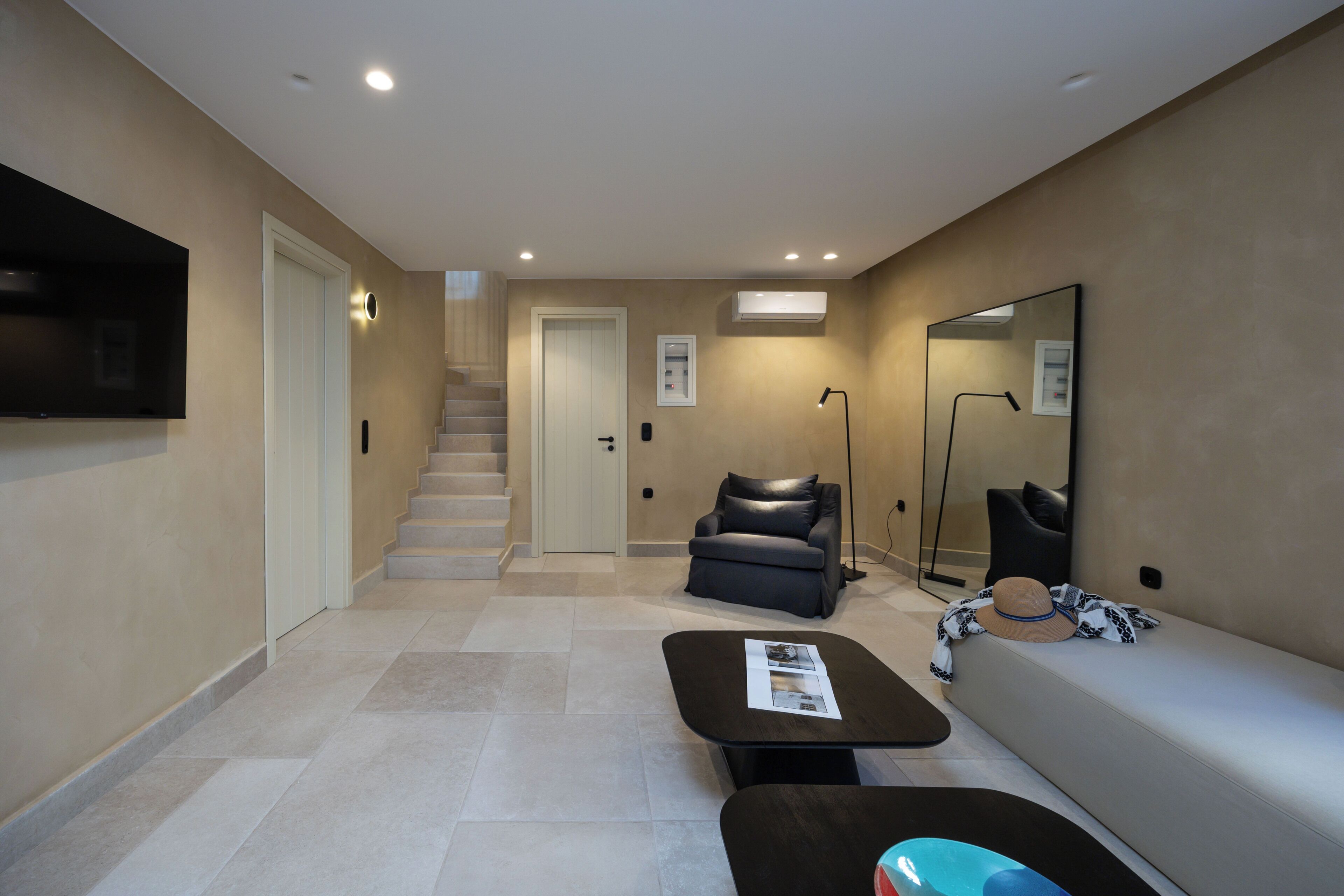 A modern living room with a flat-screen TV, a sofa, a coffee table, a chair, and a staircase leading to another room.