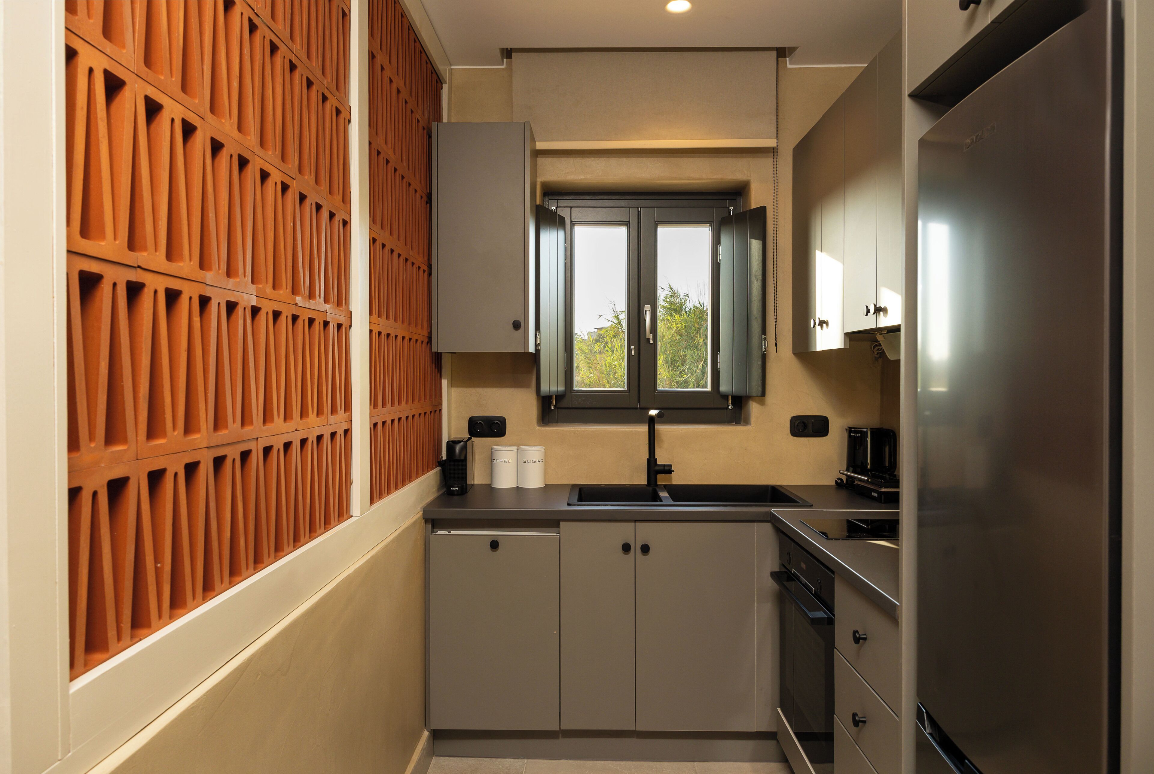 A compact kitchen with a built-in refrigerator, a window above the sink, and a wooden panel wall.