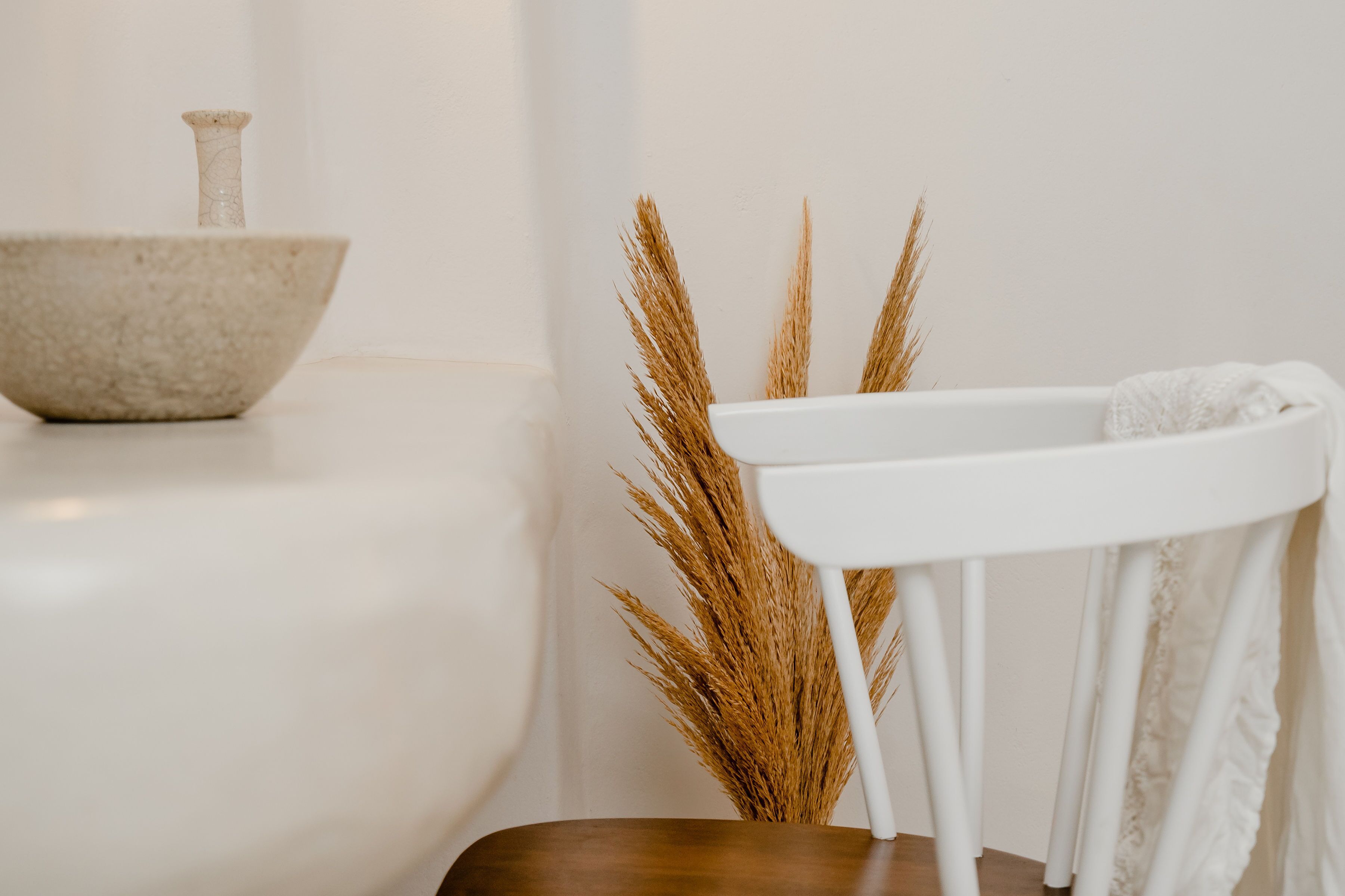 Um banheiro minimalista com uma bacia branca, um banquinho de madeira e uma planta decorativa.