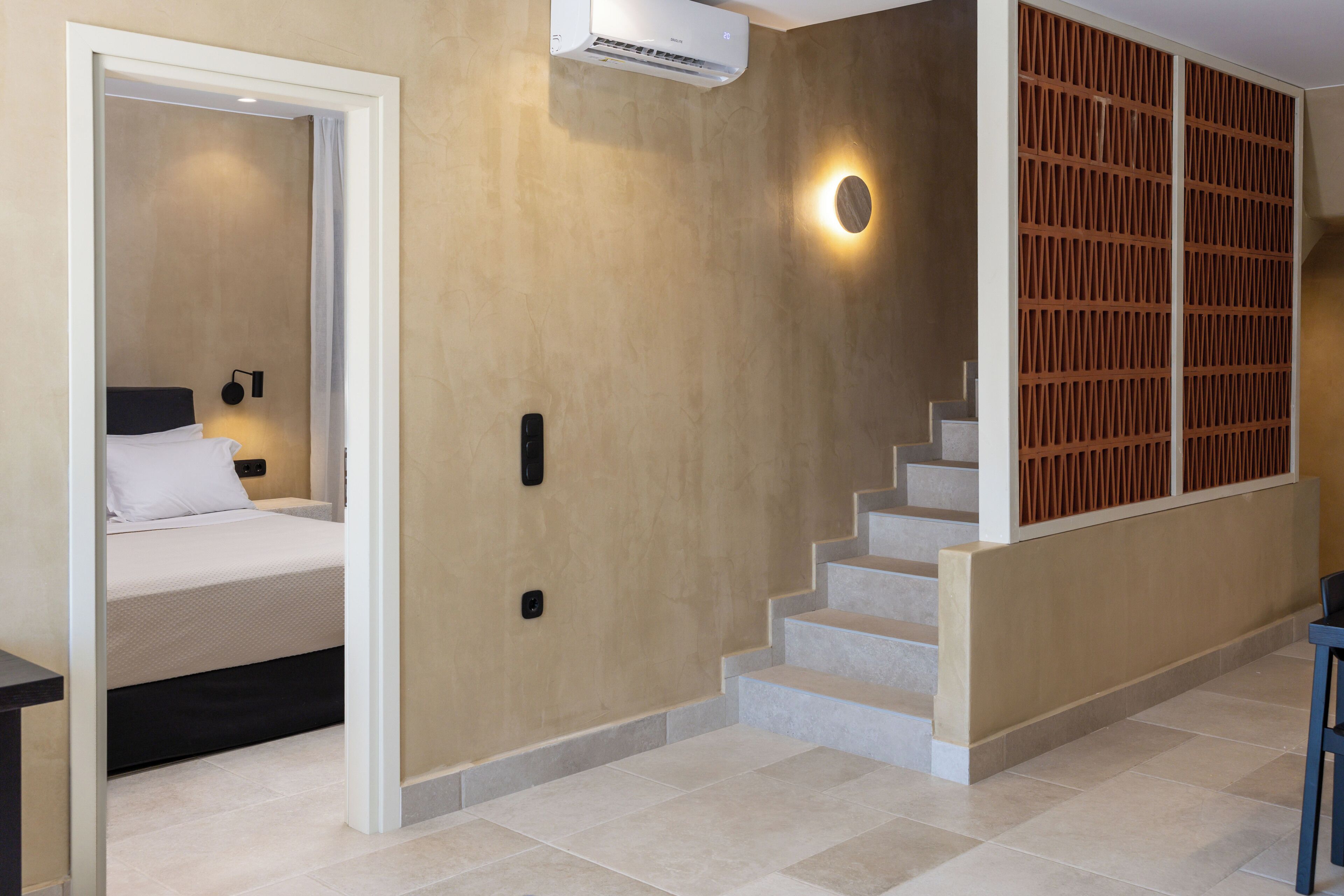 A hotel room with a bed, a desk, a chair, a staircase, and a wall-mounted air conditioner.