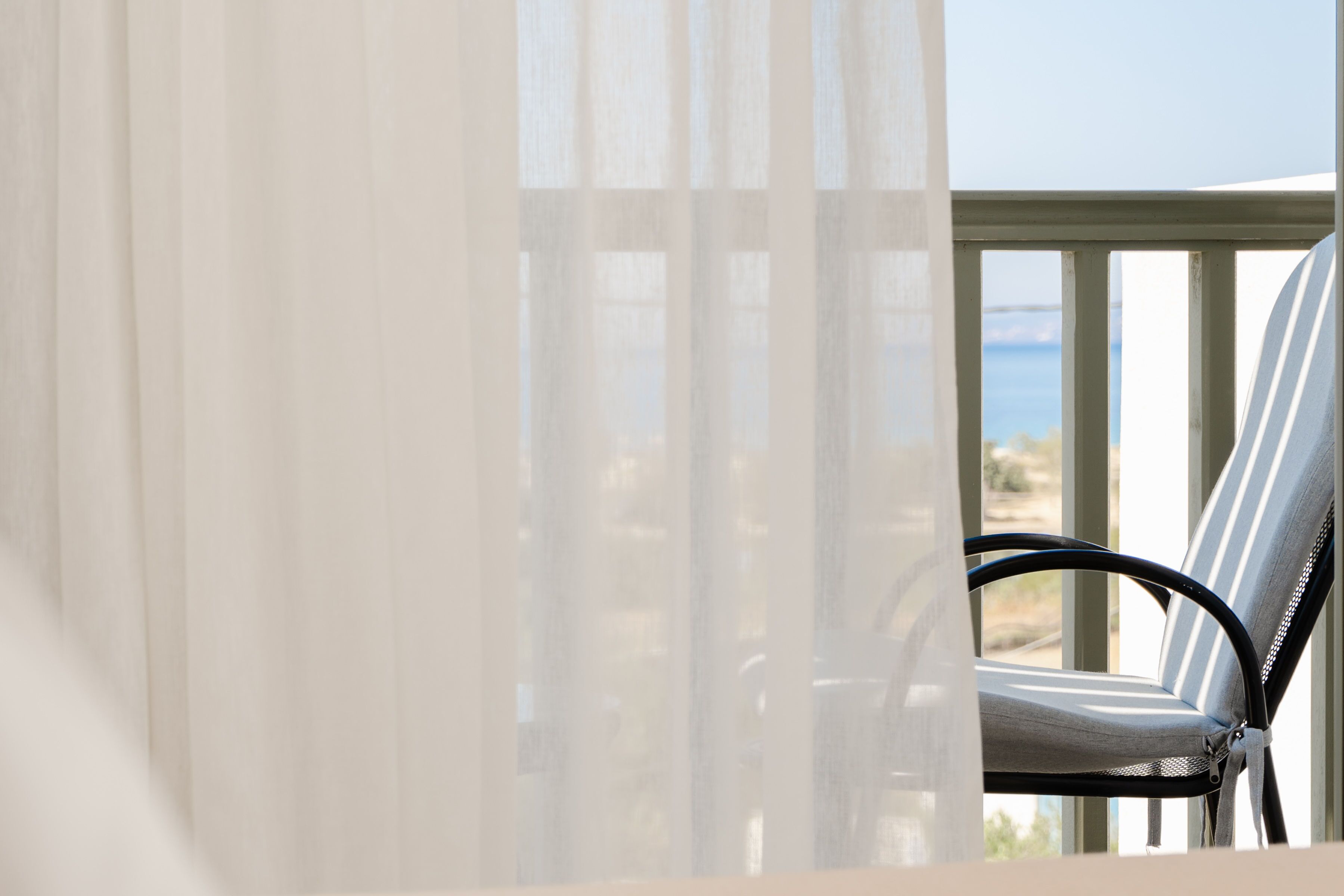 Un balcon donnant sur la mer, une chaise et de fines rideaux.