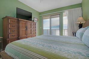 A bedroom with a large bed, a dresser, a television, and a balcony with a view.