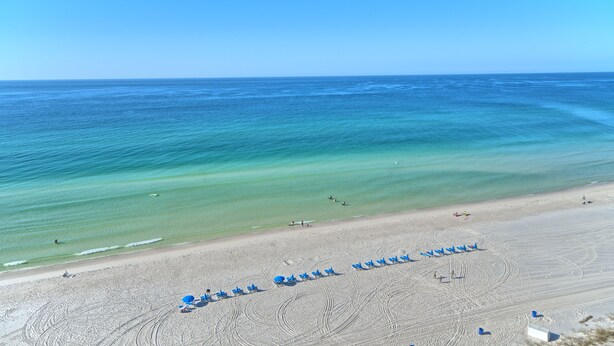 A beach with rows of blue beach chairs and umbrellas, a sandy shore, and the ocean. - Luxurious Beachfront Condo with Beachside Pool Access and Free WiFi - Unit 1202 by RedAwning (Panama City Beach)
