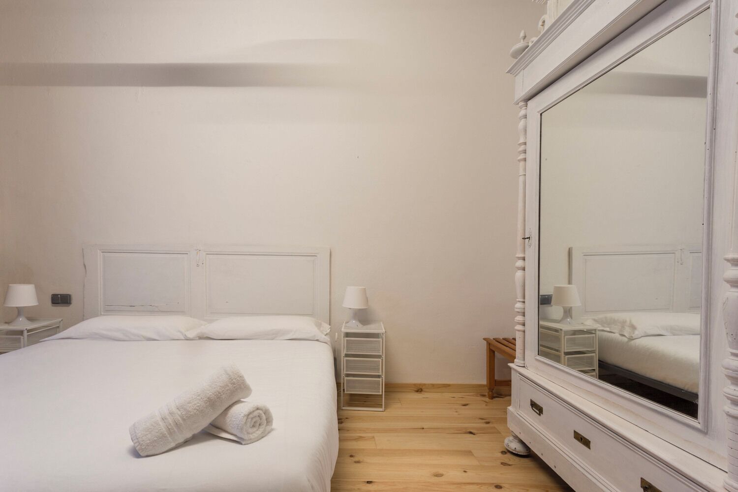 Une chambre à coucher bien rangée, avec un grand lit, deux tables de chevet, un miroir et une armoire.