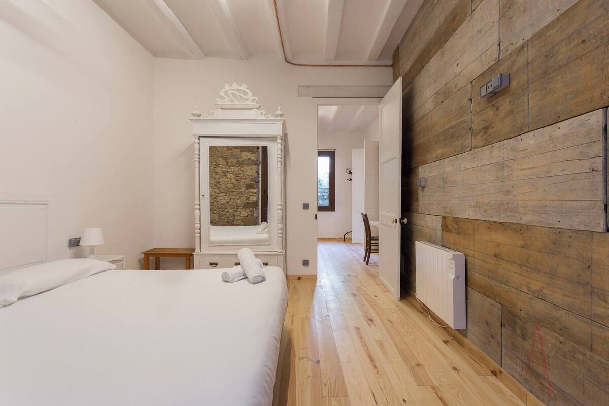 A bedroom with a large bed, a wooden wall, a stone fireplace, and a hallway leading to another room.