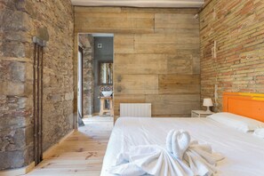 A bedroom with a wooden floor, a bed with white bedding, a wooden headboard, and a brick wall. - AS Sant Domenec Pool&Bike (Girona)