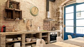Een landelijke keuken met een bakstenen muur, houten kastjes, een klok en een blauwe deur.