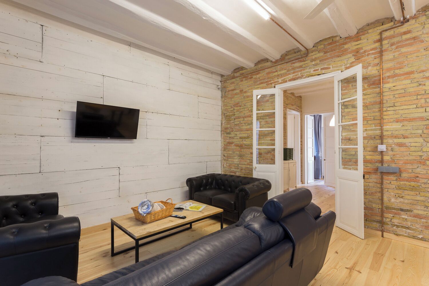 Een moderne woonkamer met een bakstenen muur, een flatscreen televisie, leren banken en een houten salontafel.