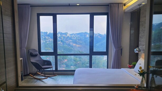 A bedroom with a large window, a bed, a chair, and a bathtub with flowers. - The Luxe Hotel Da Lat (Xuan Huong - Da Lat)