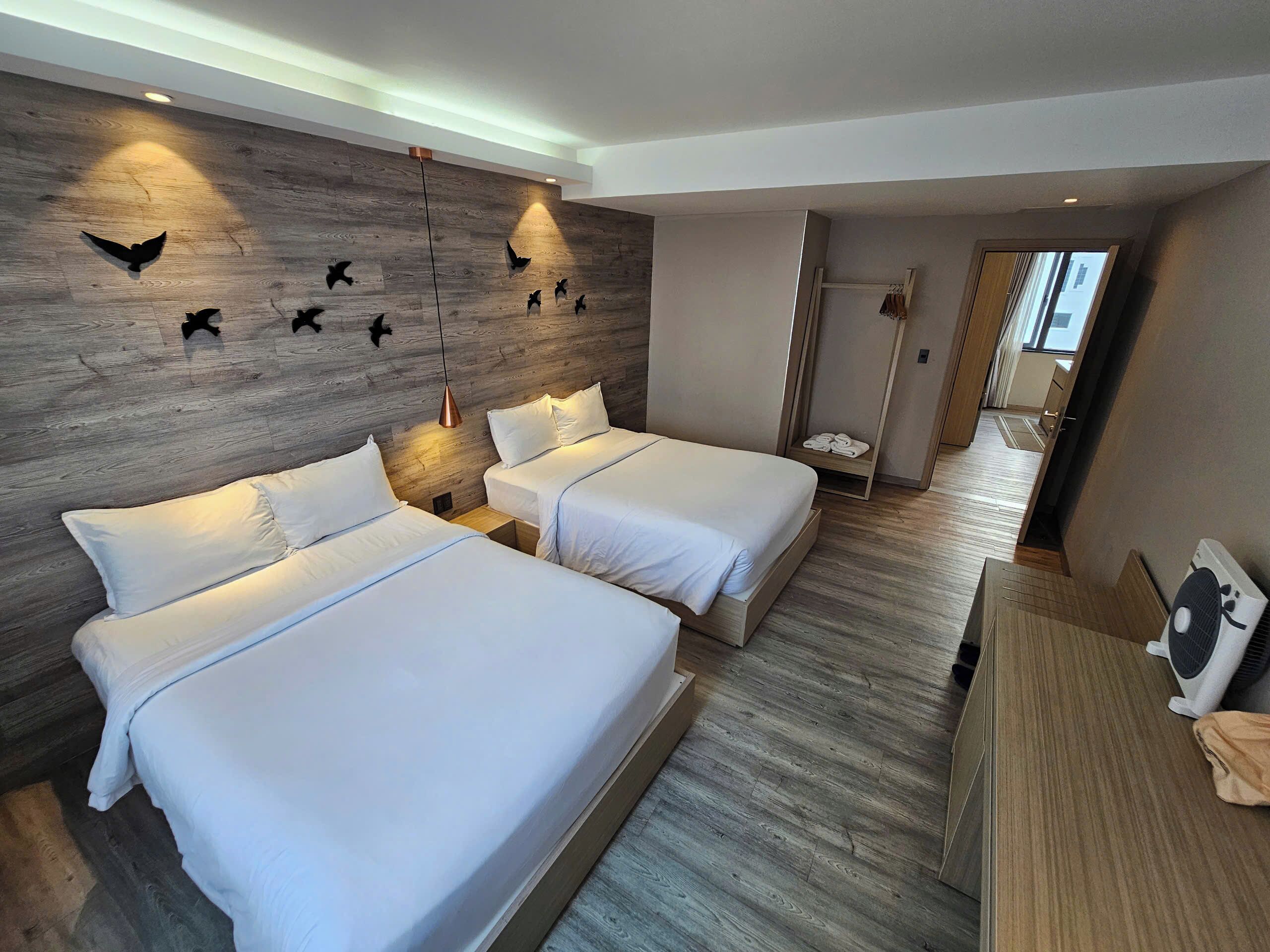 A hotel room with two beds, a wooden wall with bird silhouettes, a mirror, and a fan.