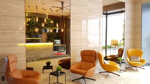 A modern lobby with a reception desk, seating area with orange and yellow chairs, and a ceiling fan. - The Luxe Hotel Da Lat (Xuan Huong - Da Lat)